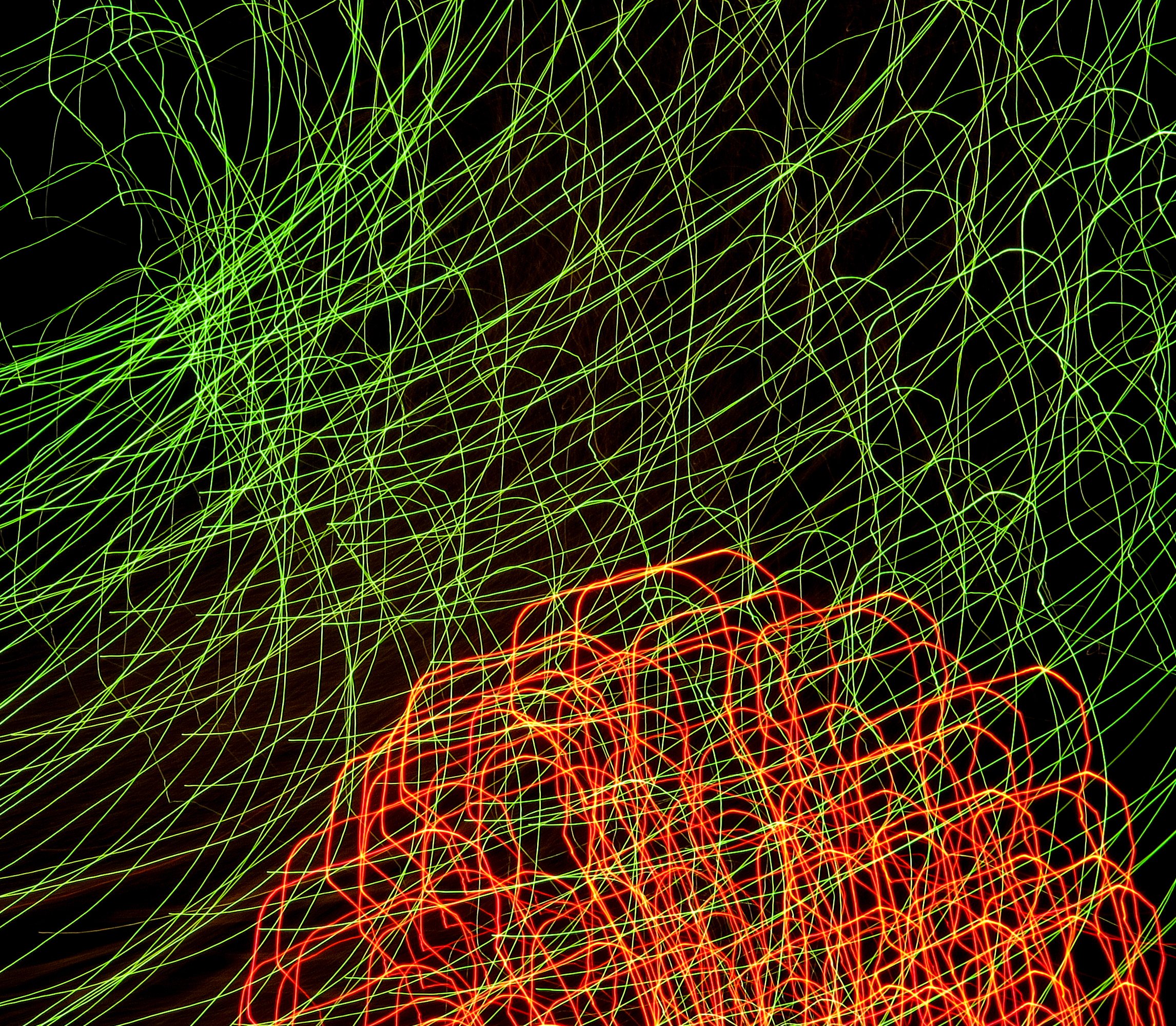 Abstract long-exposure light painting with neon green and red tangled lines on a black background