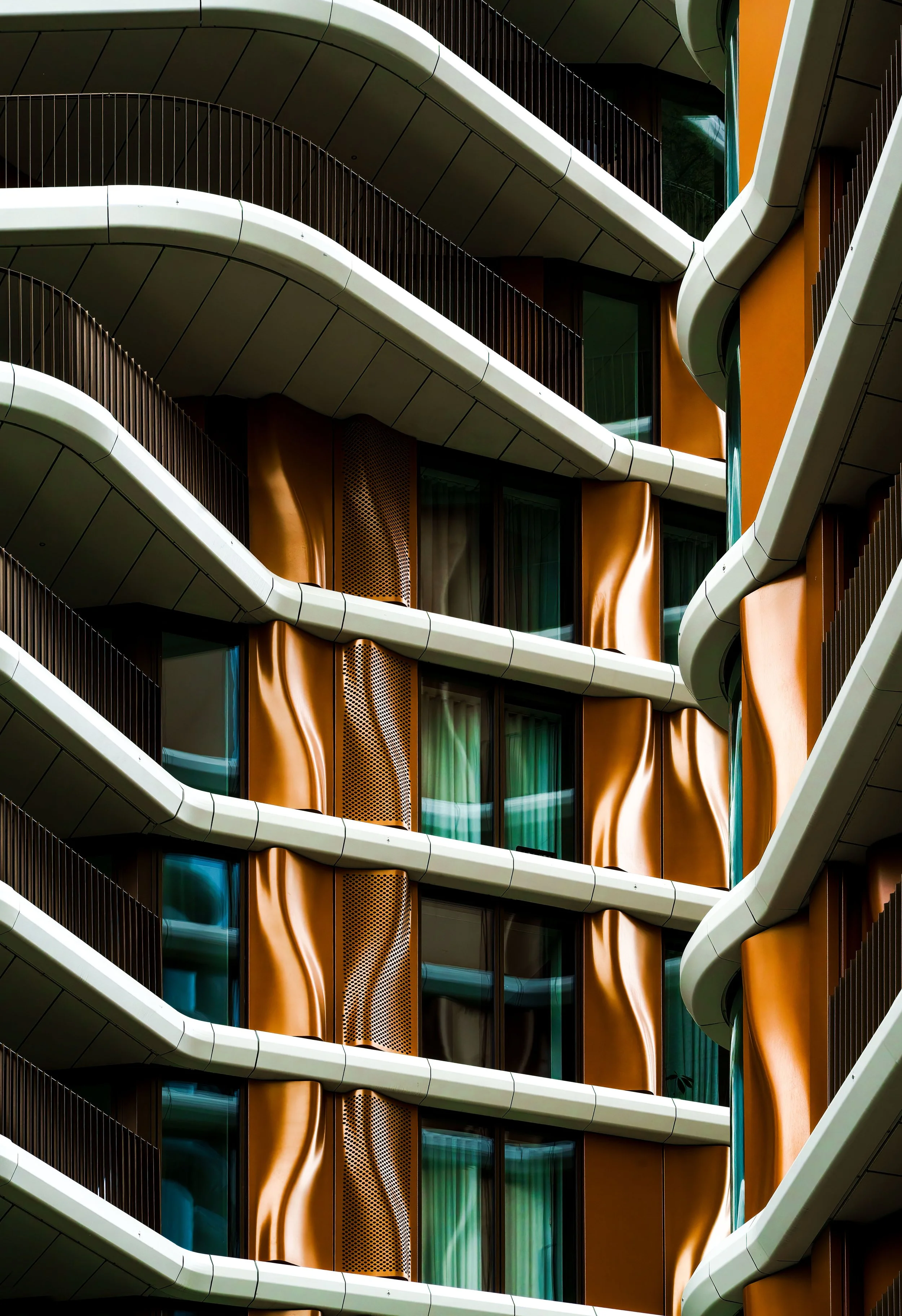 Modern building facade with sweeping white balconies, copper-colored panels, dark vertical slats, and reflective windows