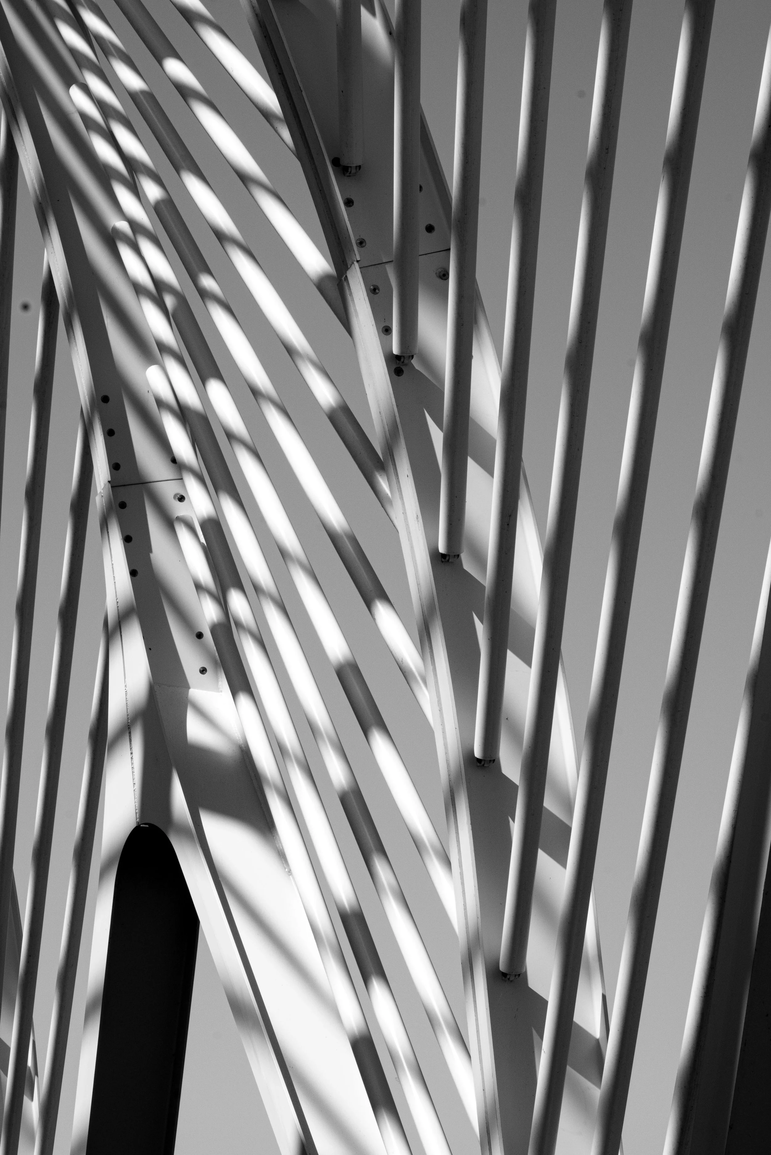 Black-and-white close-up of white metal architectural beams and columns casting geometric shadows.