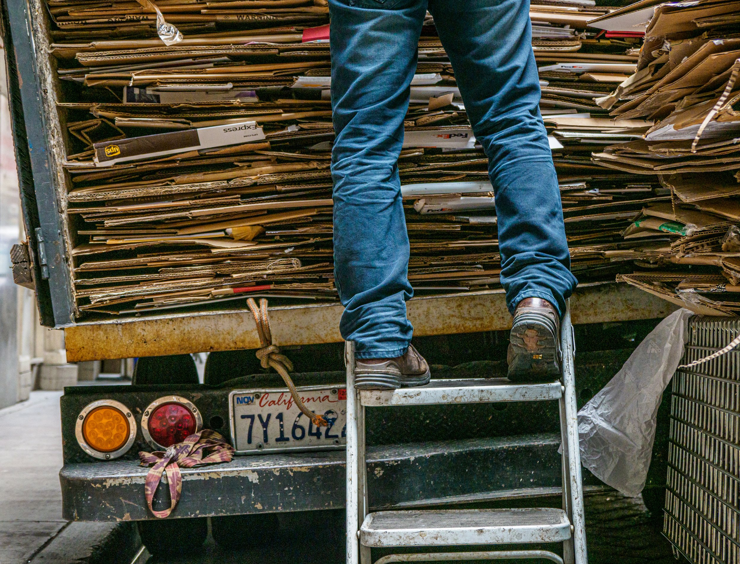 Worker standing on a ladder beside a truck loaded with flattened cardboard for recycling