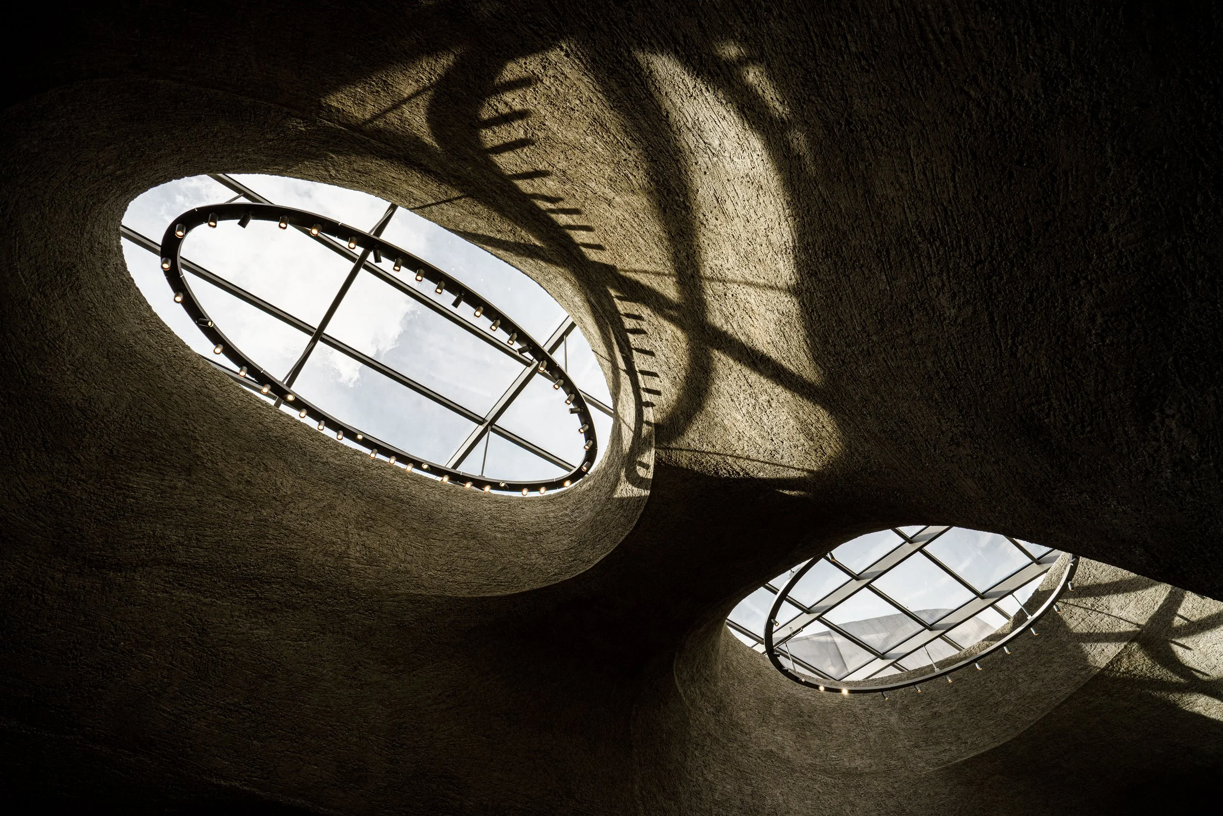 Curved textured concrete interior with oval skylights, metal framing, and rows of small lights.