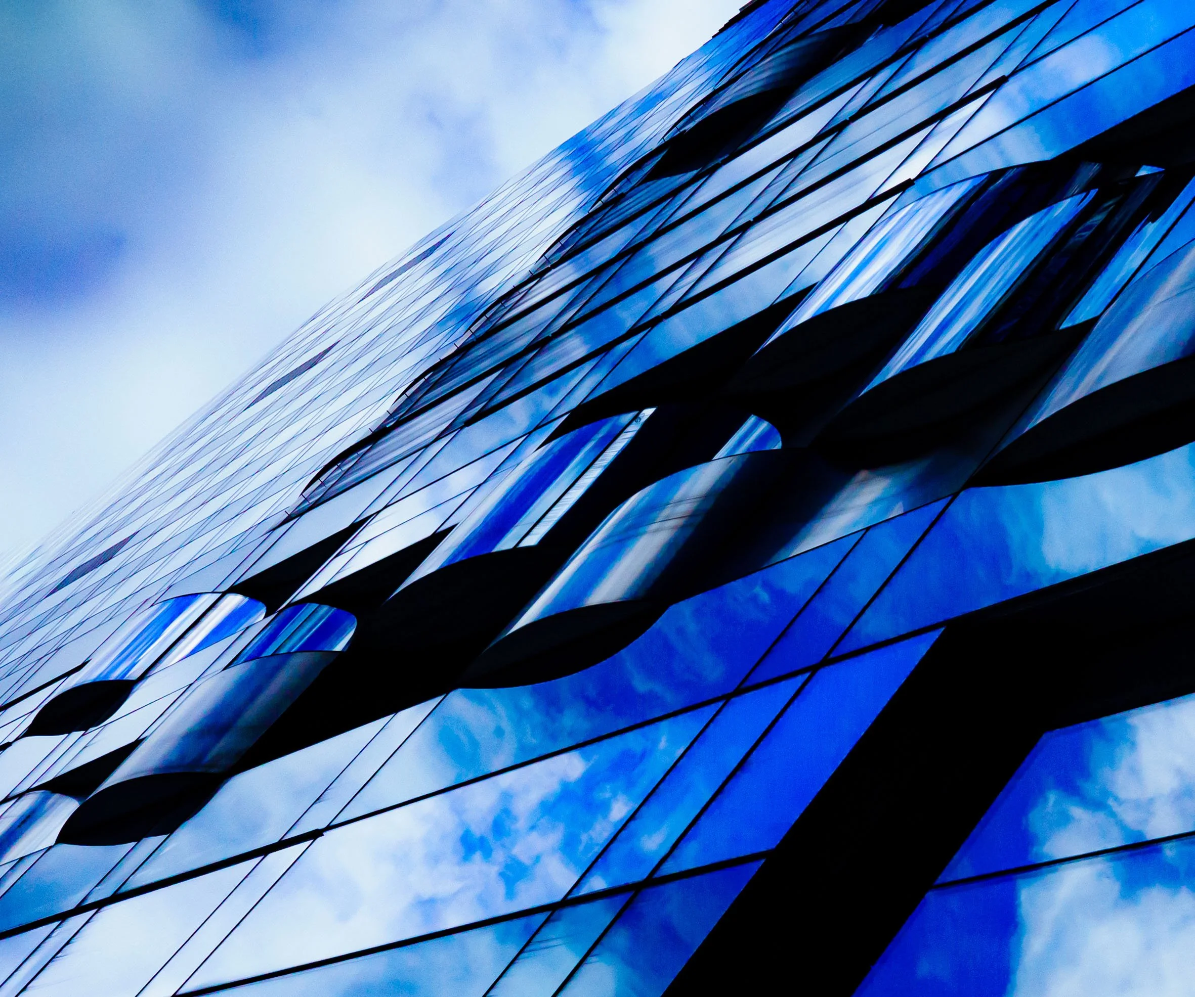 Abstract close-up of a blue glass skyscraper reflecting a cloudy sky