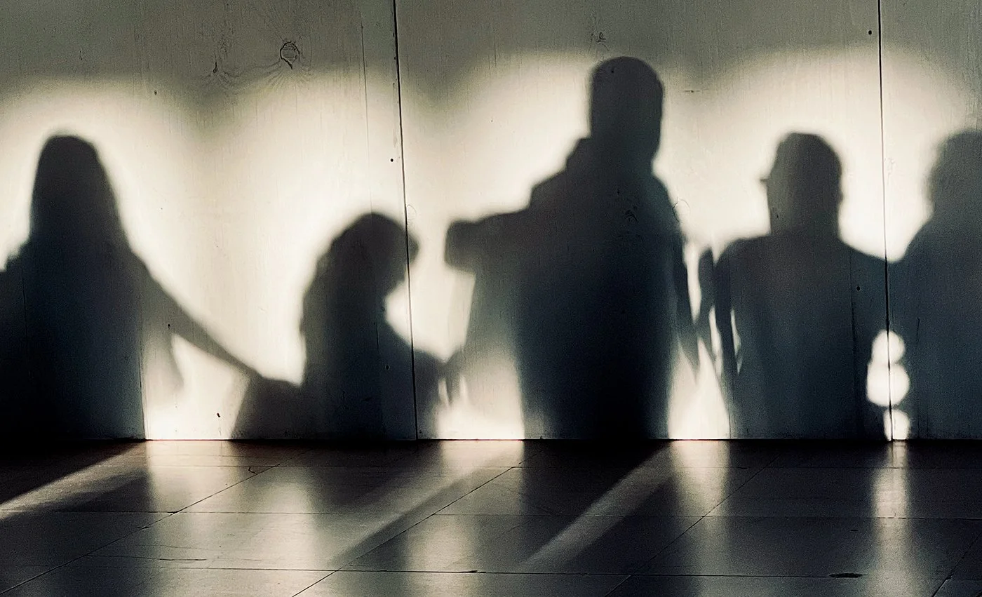 Shadows of several people projected onto a sunlit wall and tiled floor