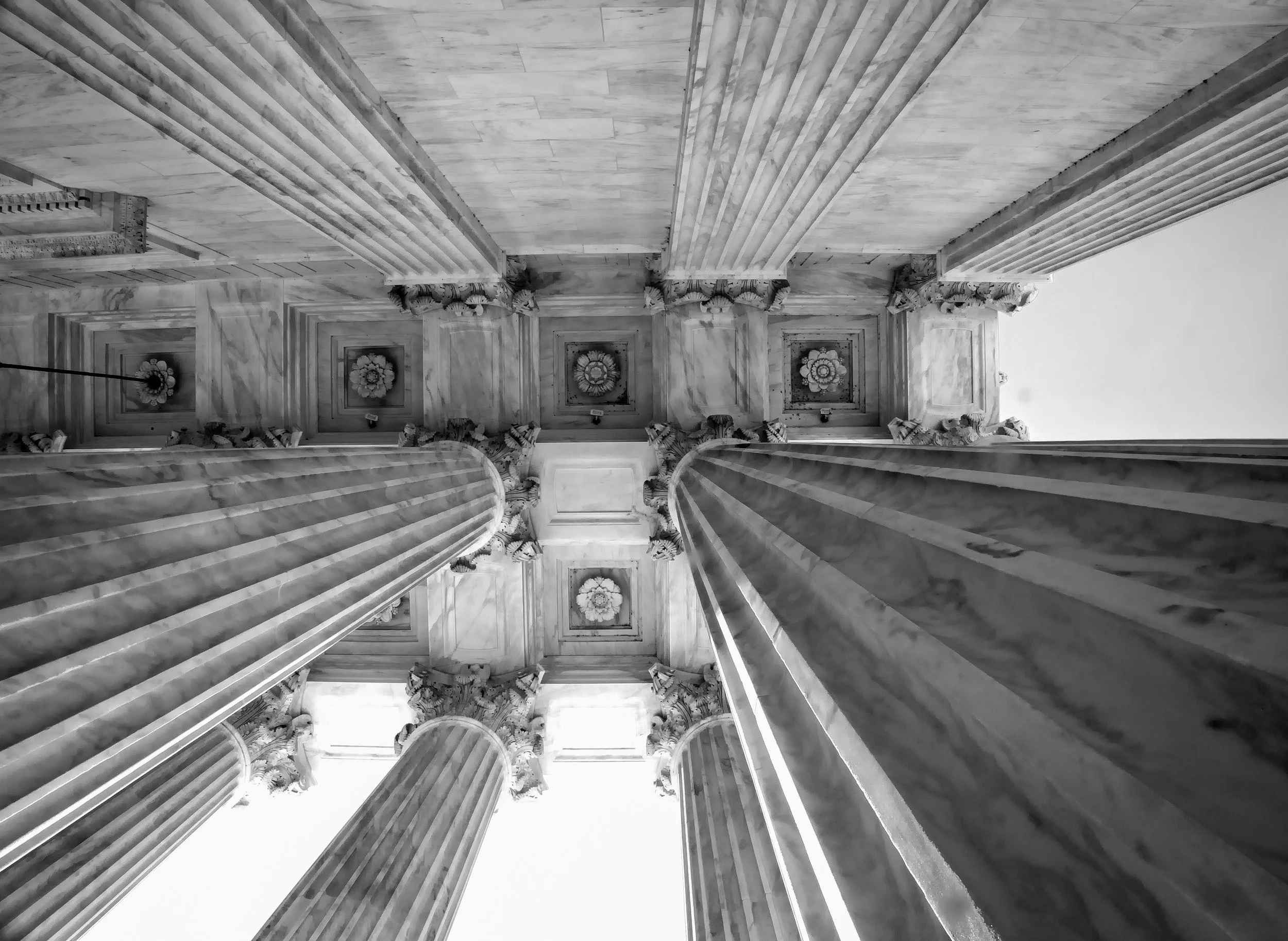 Black-and-white upward view of ornate Baroque church columns, carved capitals, and decorative ceiling rosettes