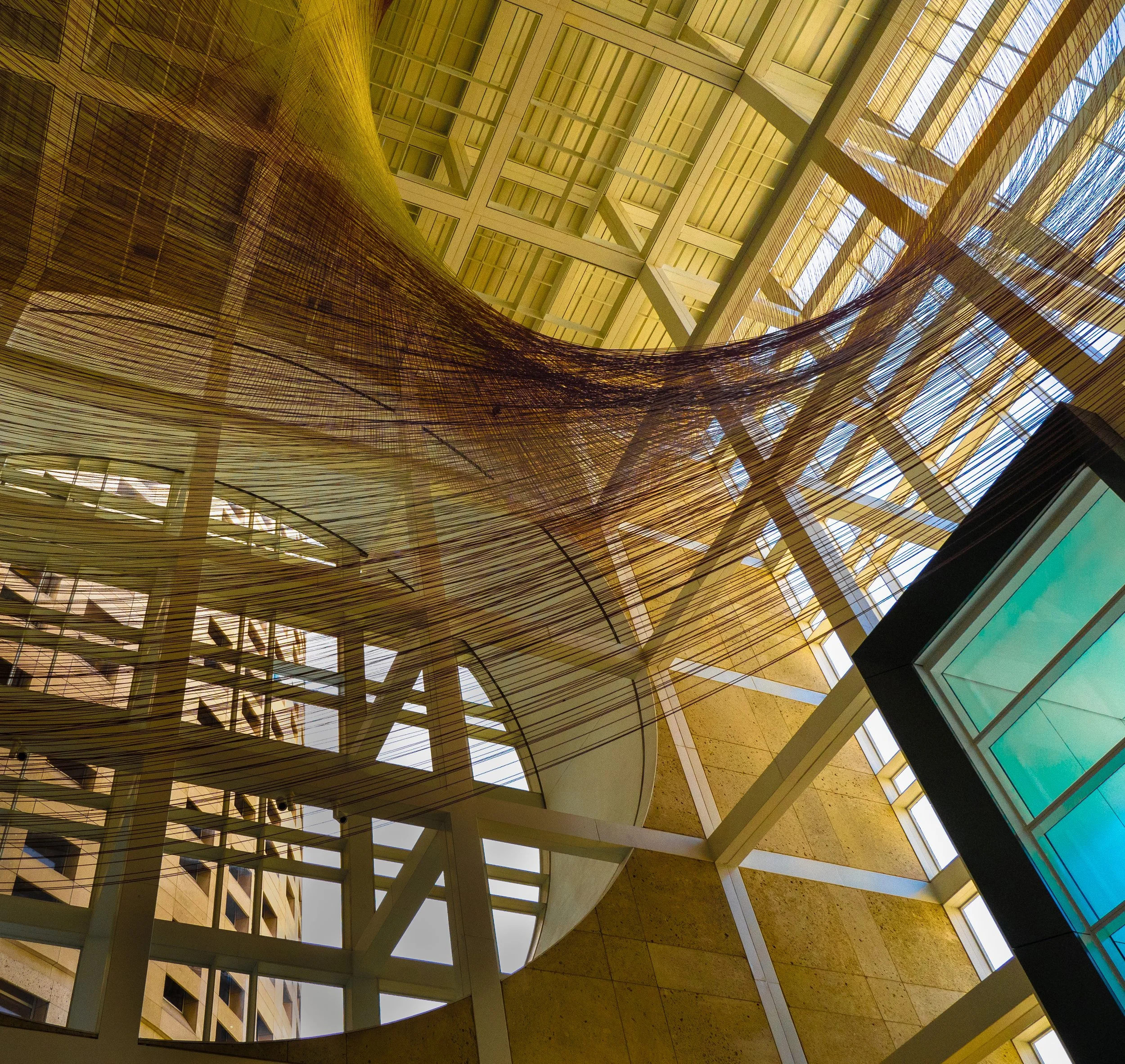 Abstract modern atrium interior with geometric skylights, structural beams, and suspended woven fiber installation