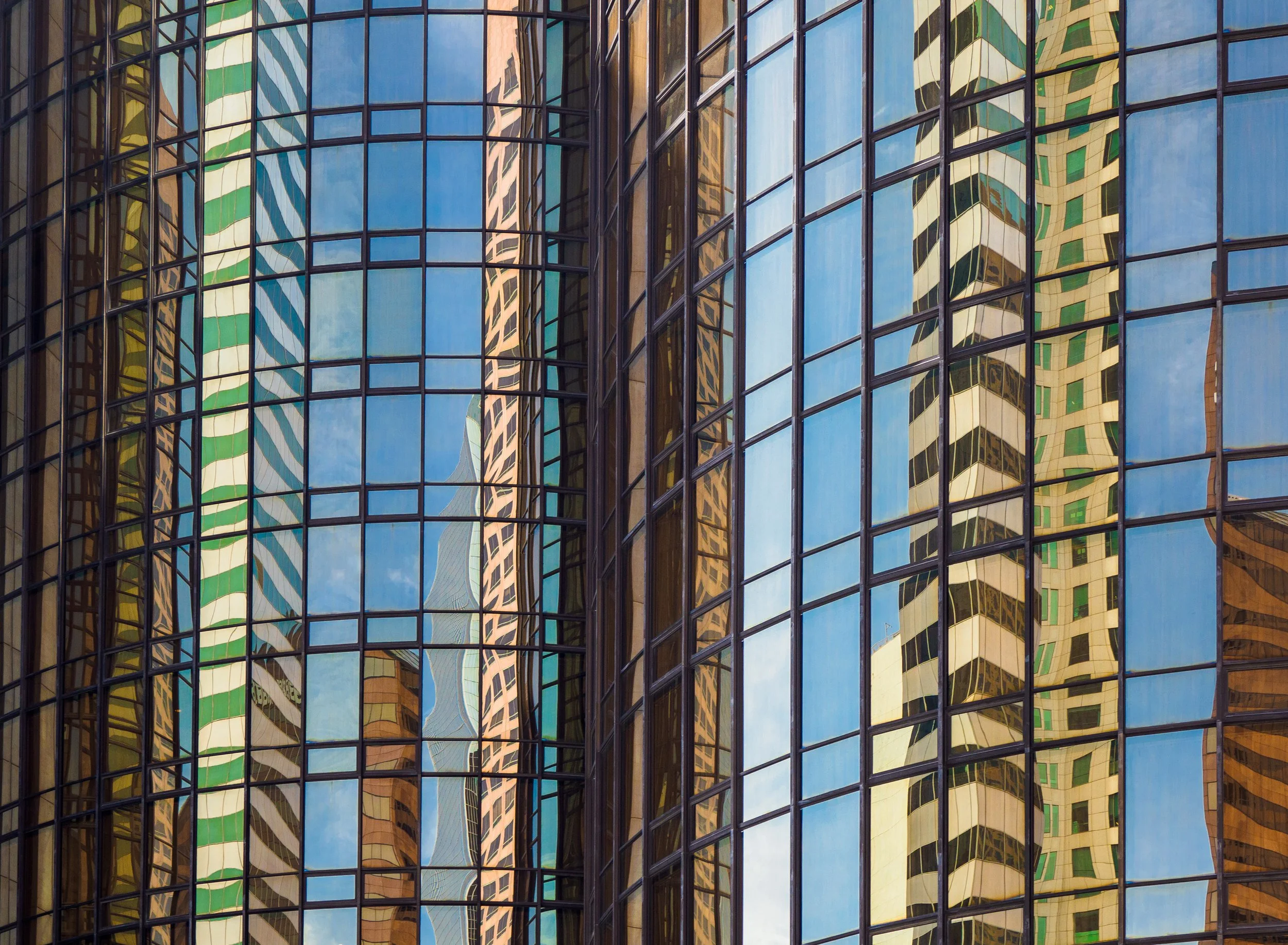 Reflective glass office buildings with distorted skyscraper reflections against a blue sky