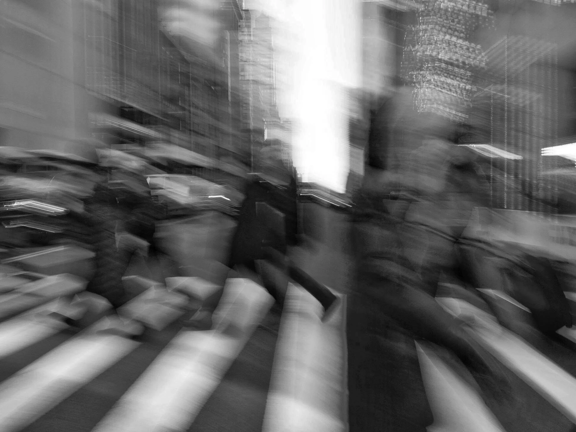 Black-and-white long-exposure photograph of blurred city traffic and pedestrians between tall buildings.