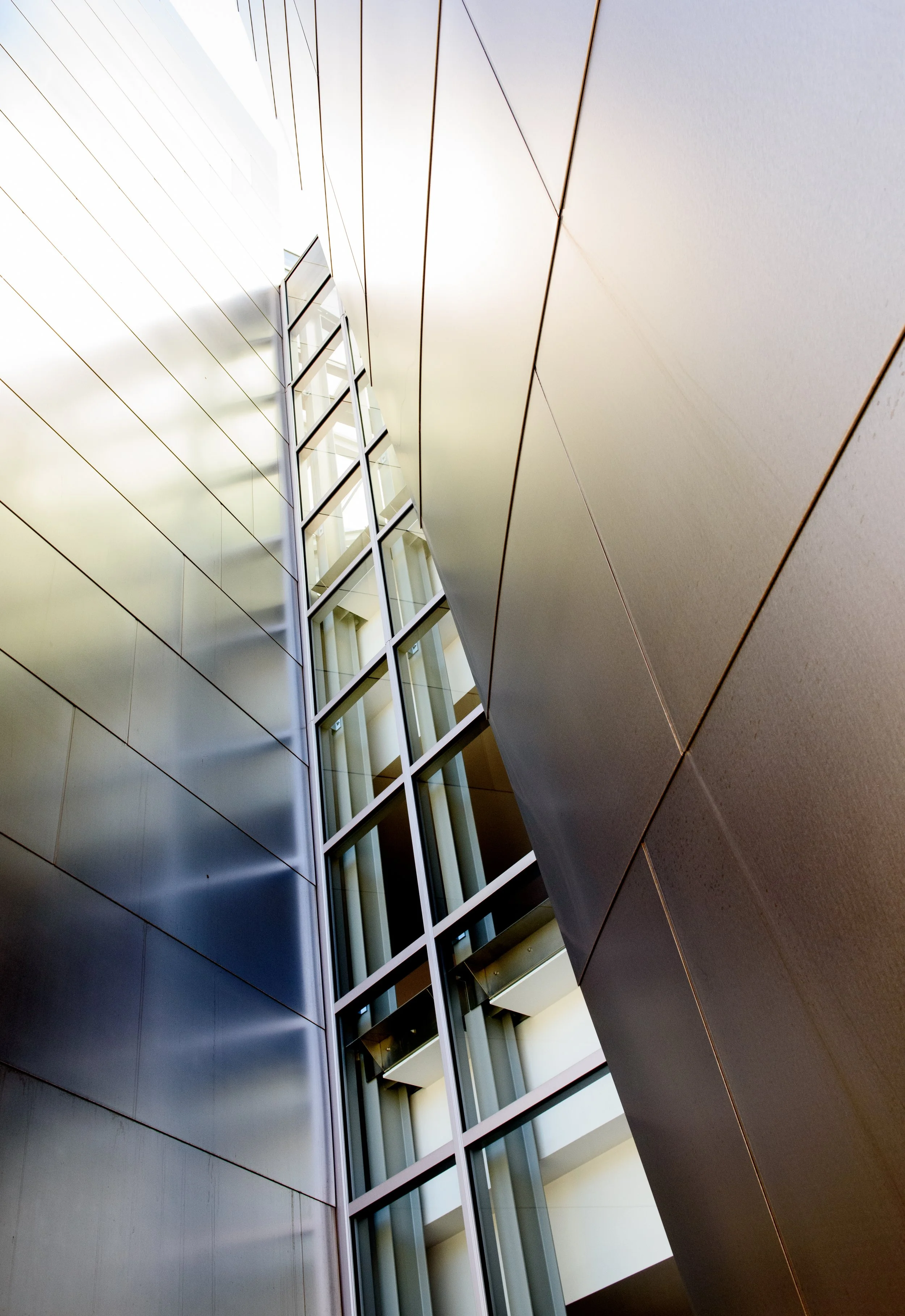 Abstract upward view of a modern building interior with geometric metal panels, glass windows, and architectural lines