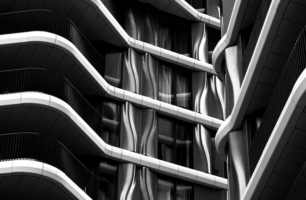 Black-and-white close-up of a modern building facade with curved balconies, window panels, and sculptural architectural details