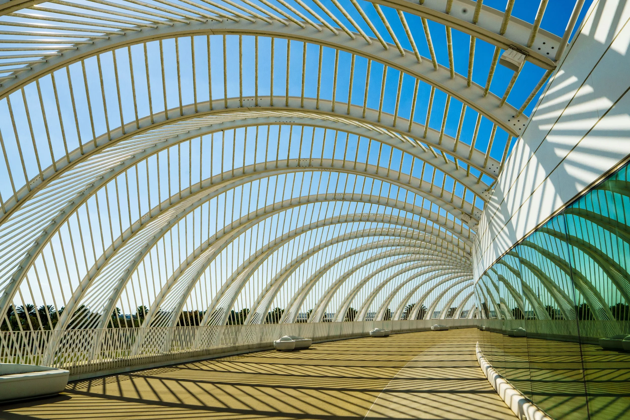 Futuristic white arched canopy over a sunlit terrace with glass walls and blue sky