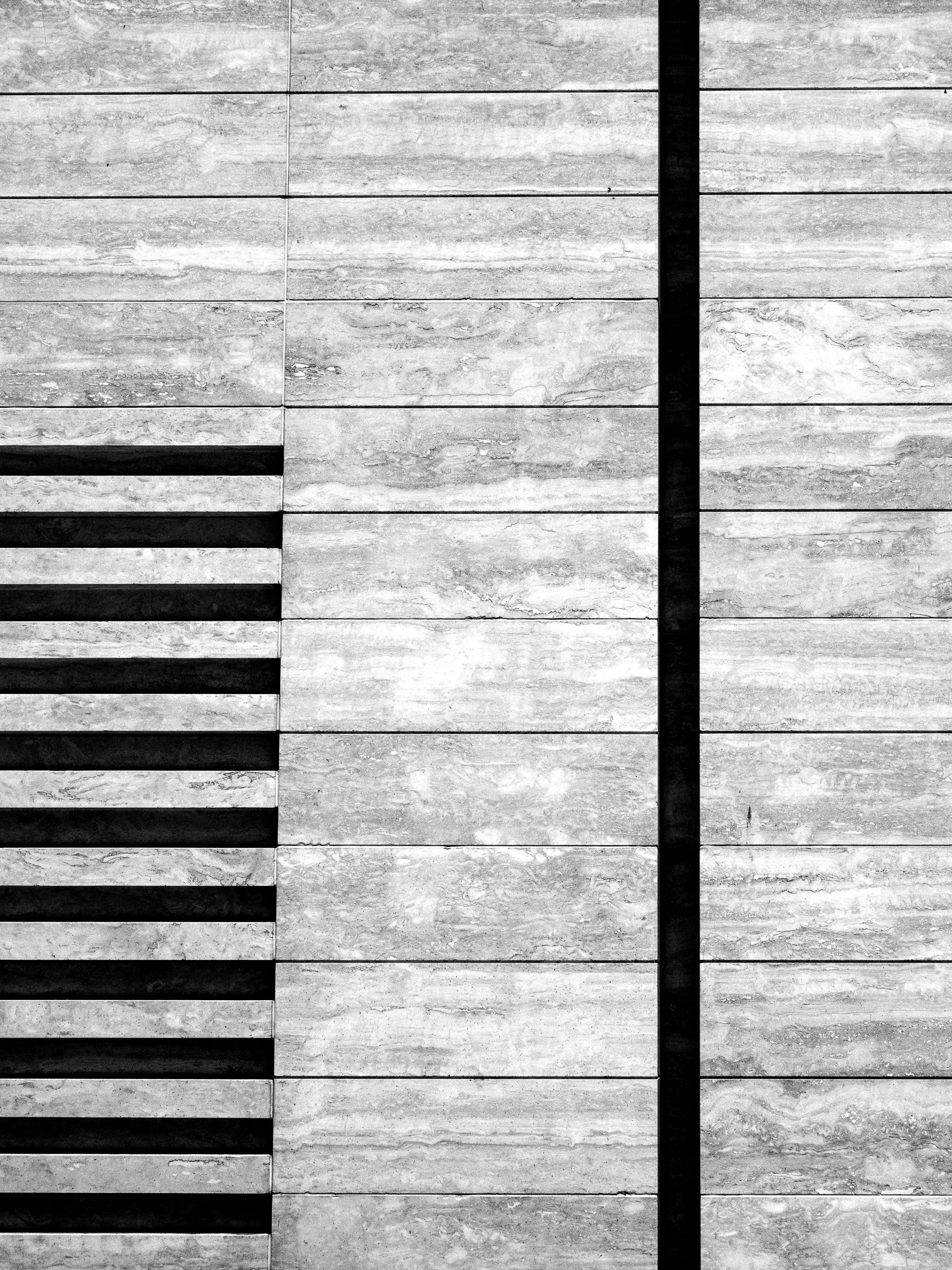 Black-and-white close-up of a geometric wall tiled with textured stone slabs and bold black grout lines.