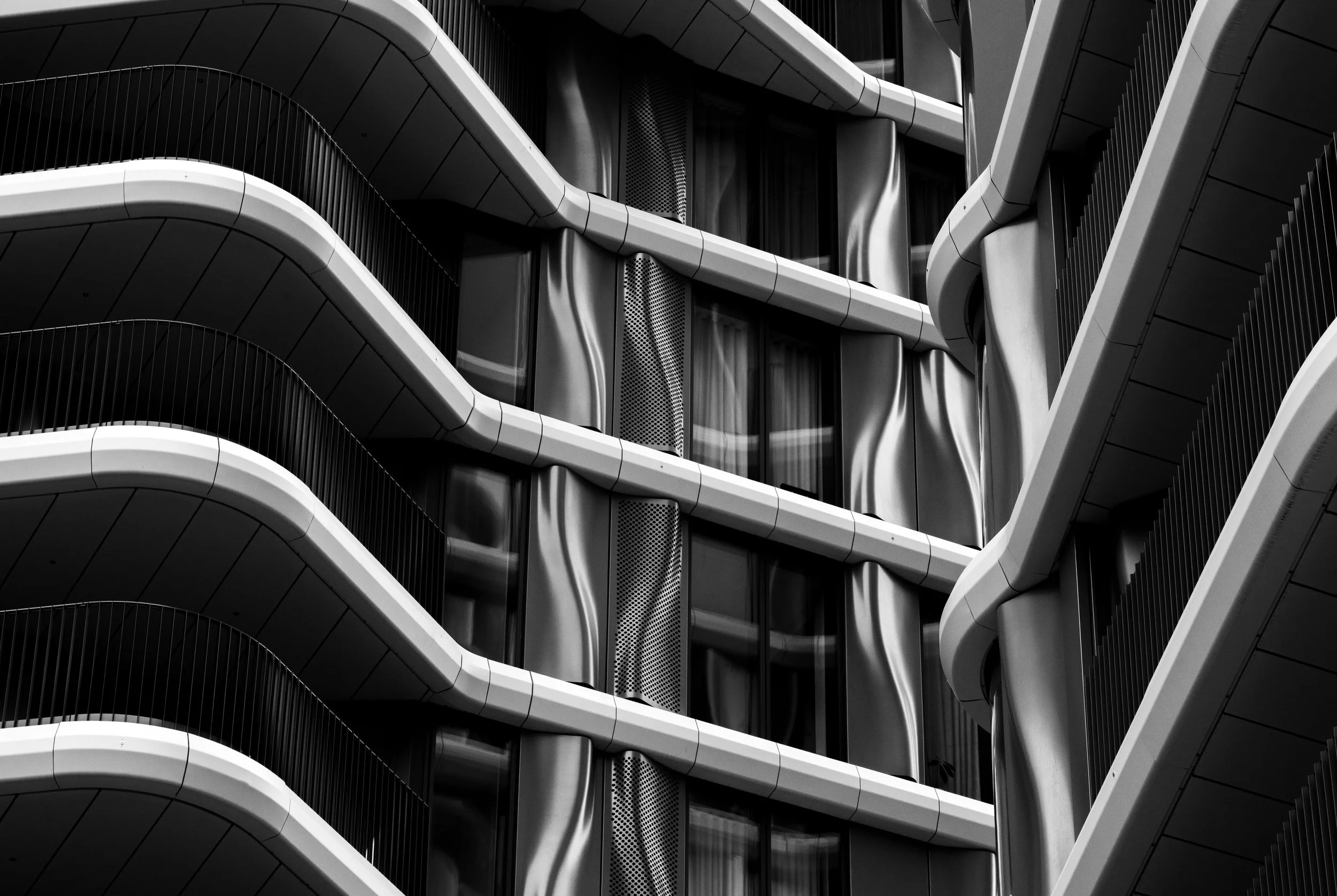 Black-and-white abstract view of a modern building facade with curved balconies, railings, and sculptural architectural beams