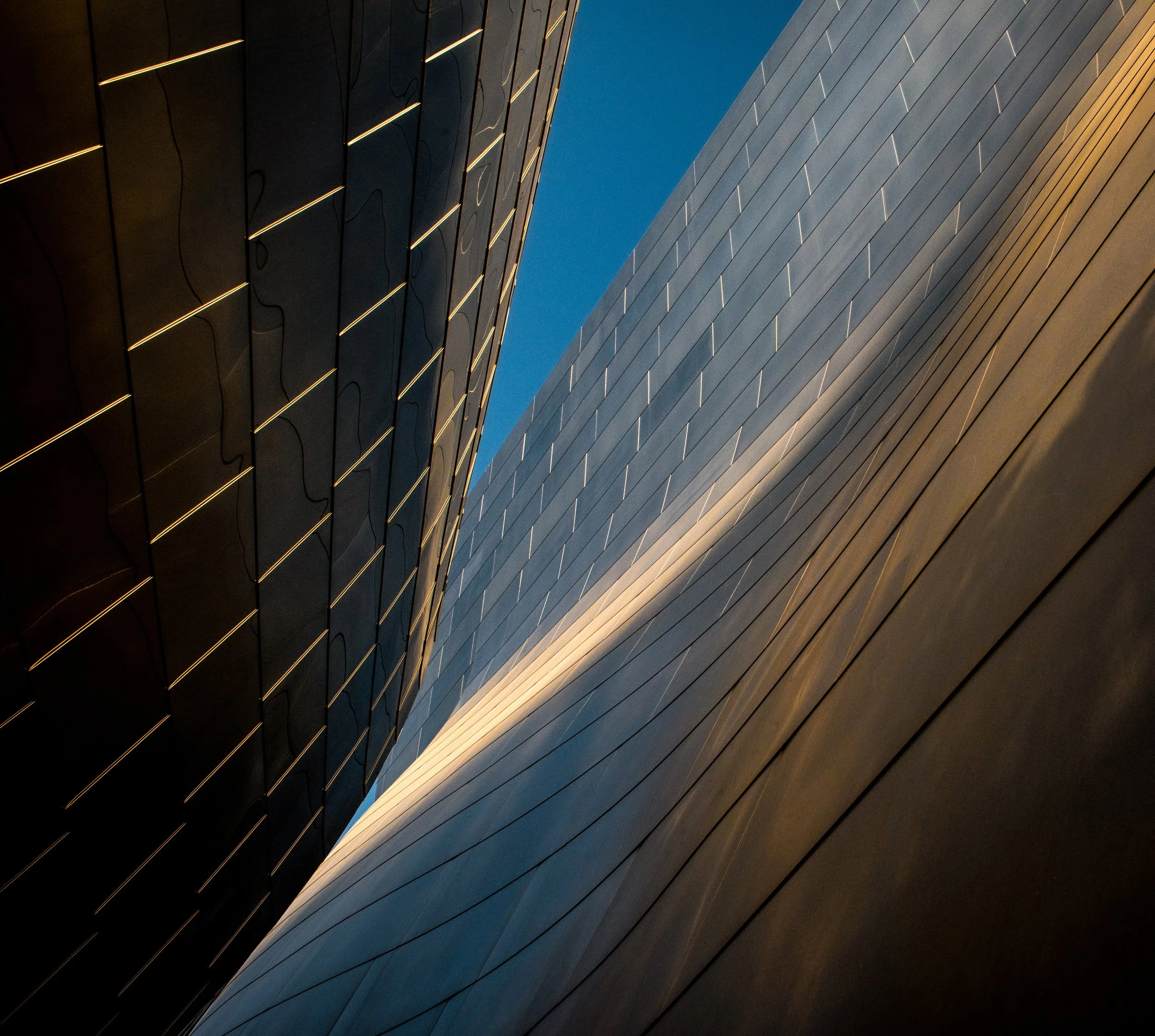 Abstract upward view between modern buildings with geometric metal facades and a blue sky