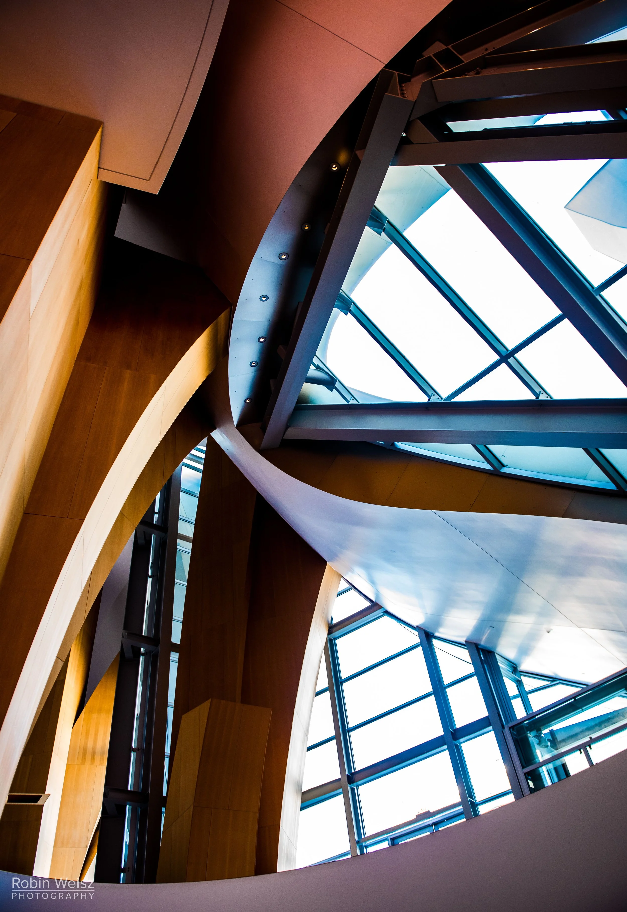 Abstract architectural interior with wood panels, steel beams, curved surfaces, and blue-tinted glass windows