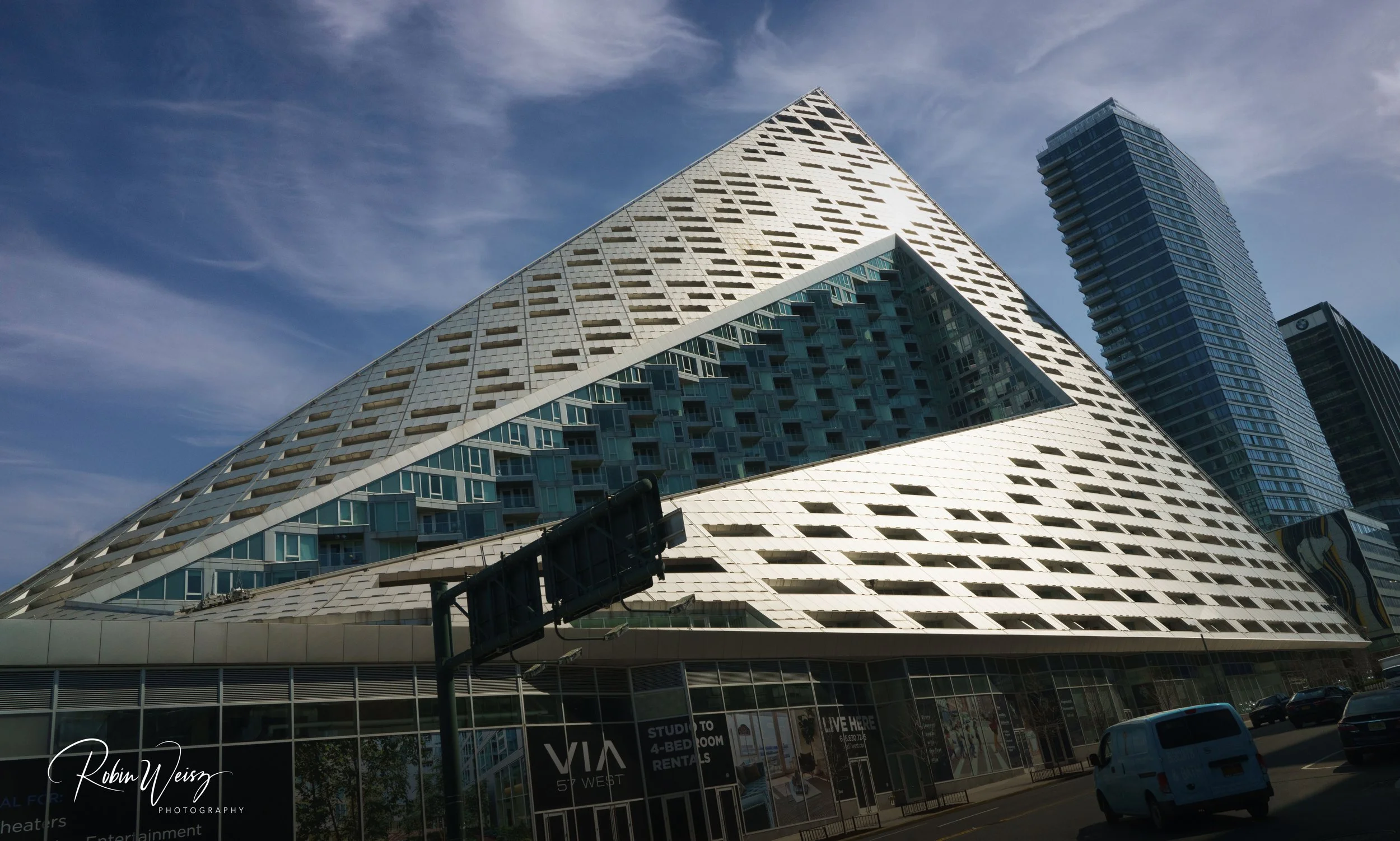 Low-angle view of the angular VIA 57 West residential building and surrounding skyscrapers in Manhattan under a cloudy blue sky