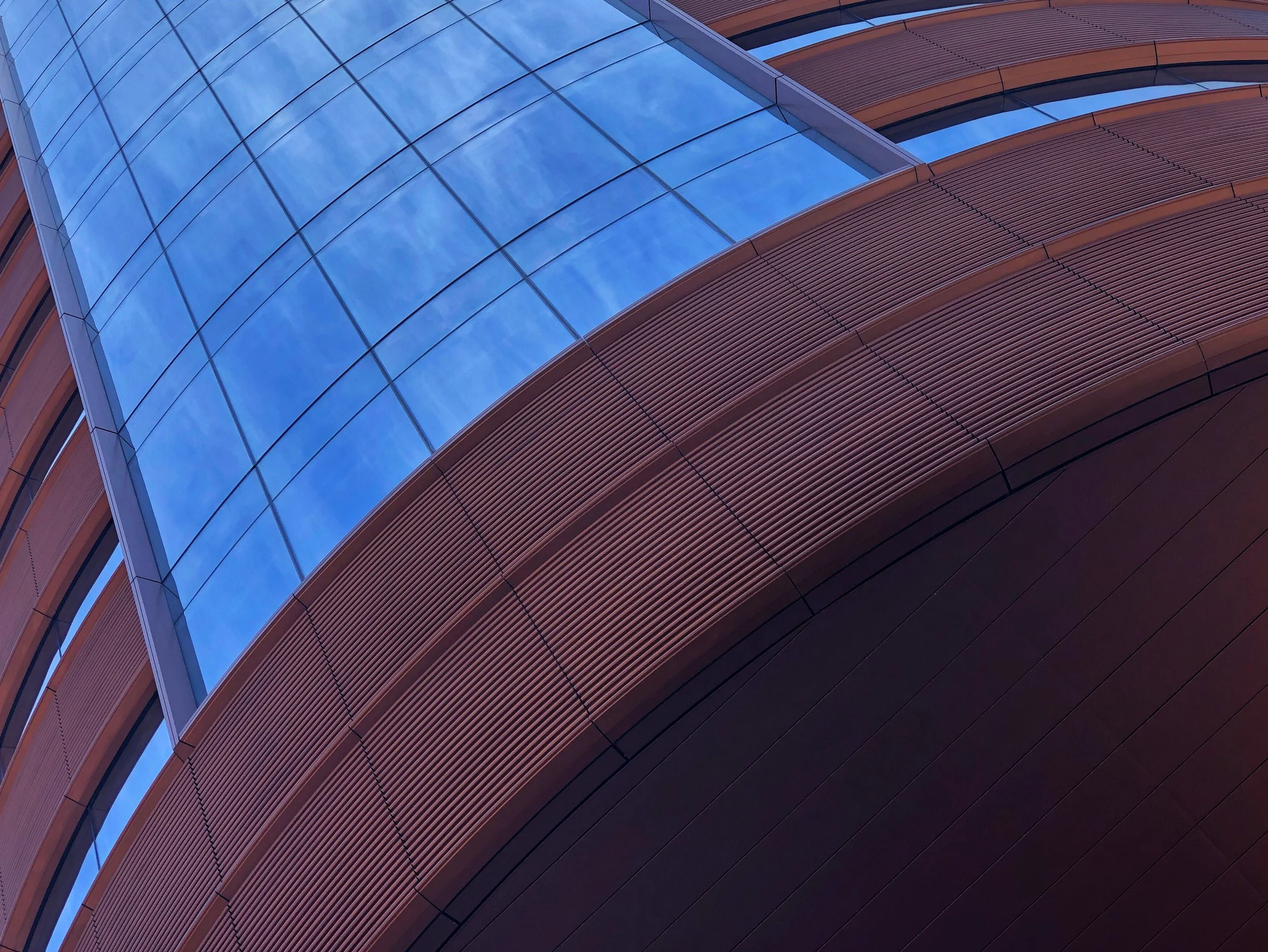 Upward view of a modern building with reflective blue glass panels and ribbed reddish-brown metal facade.