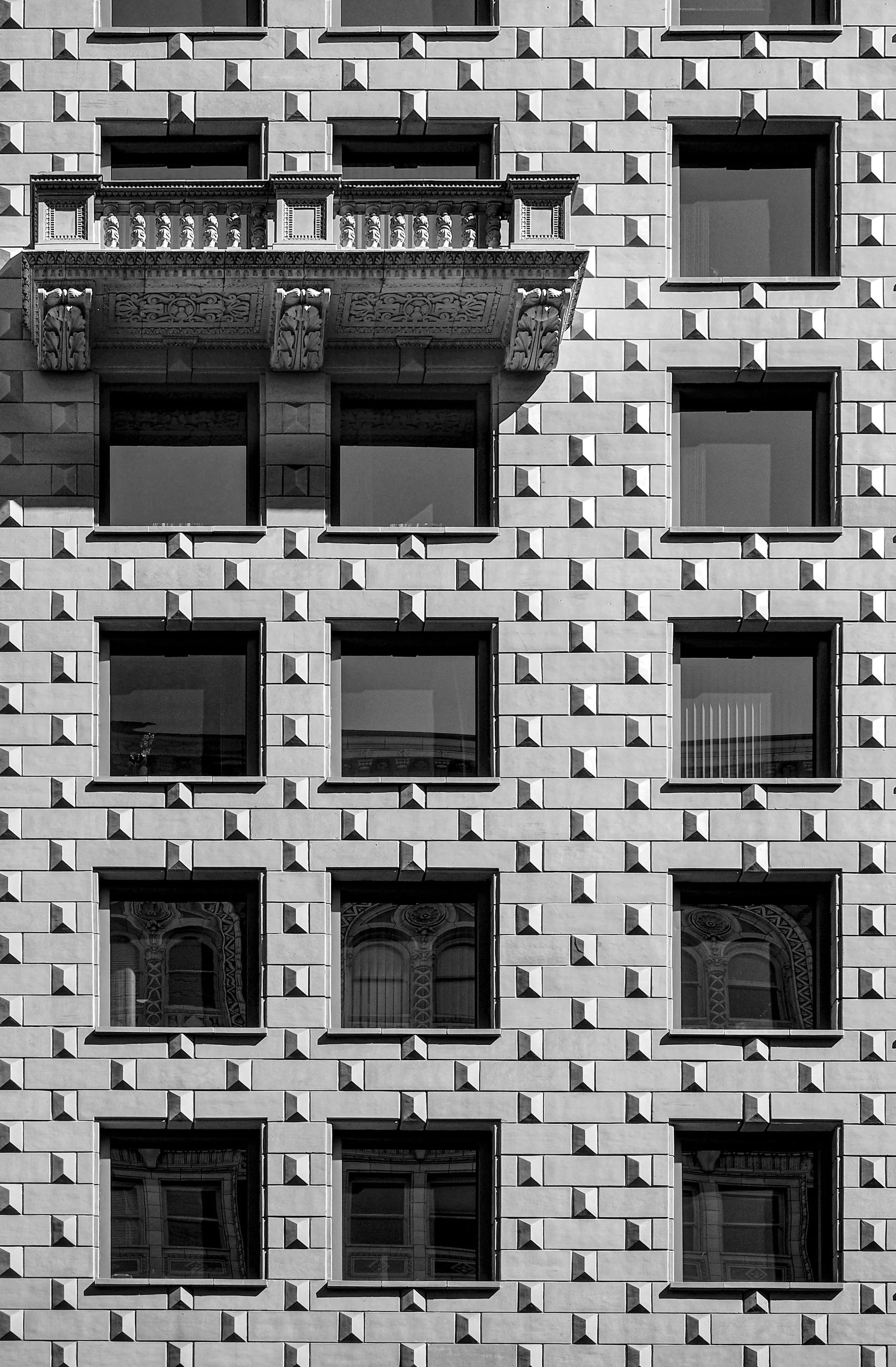 Black-and-white close-up of an ornate stone building facade with geometric masonry, recessed windows, and carved classical ornamentation