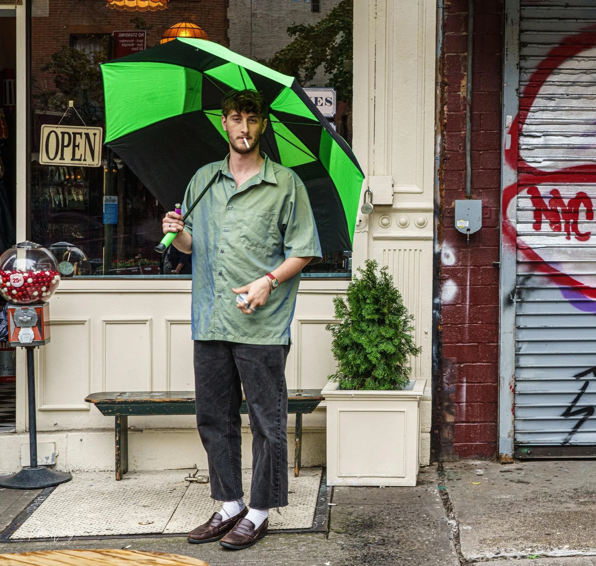 Man holding a bright green and black umbrella outside a storefront with an open sign