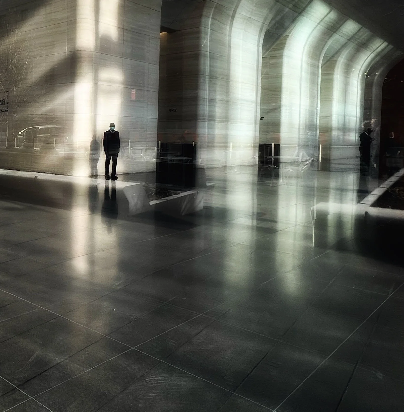 Reflective memorial interior with massive stone columns, arched walls, polished dark floor, and visitors