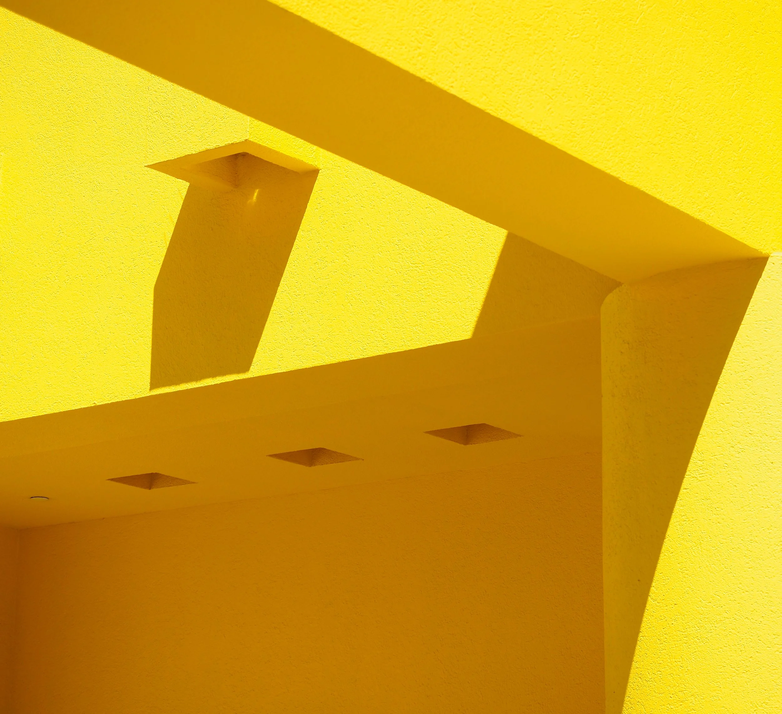 Abstract yellow architectural interior with geometric beams, columns, recessed ceiling squares, and dramatic shadows