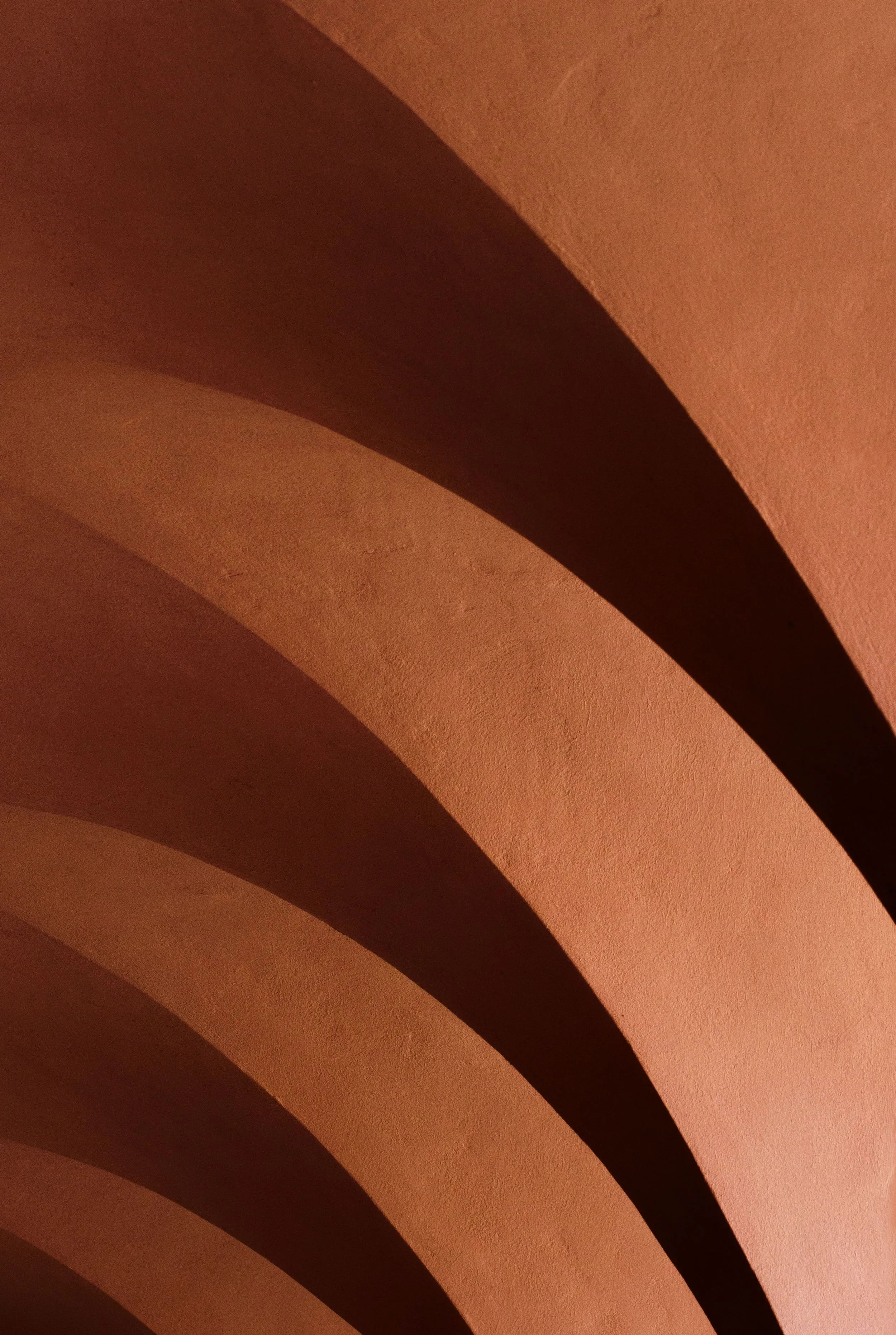 Warm sunlight casting long diagonal shadows across a textured terracotta wall