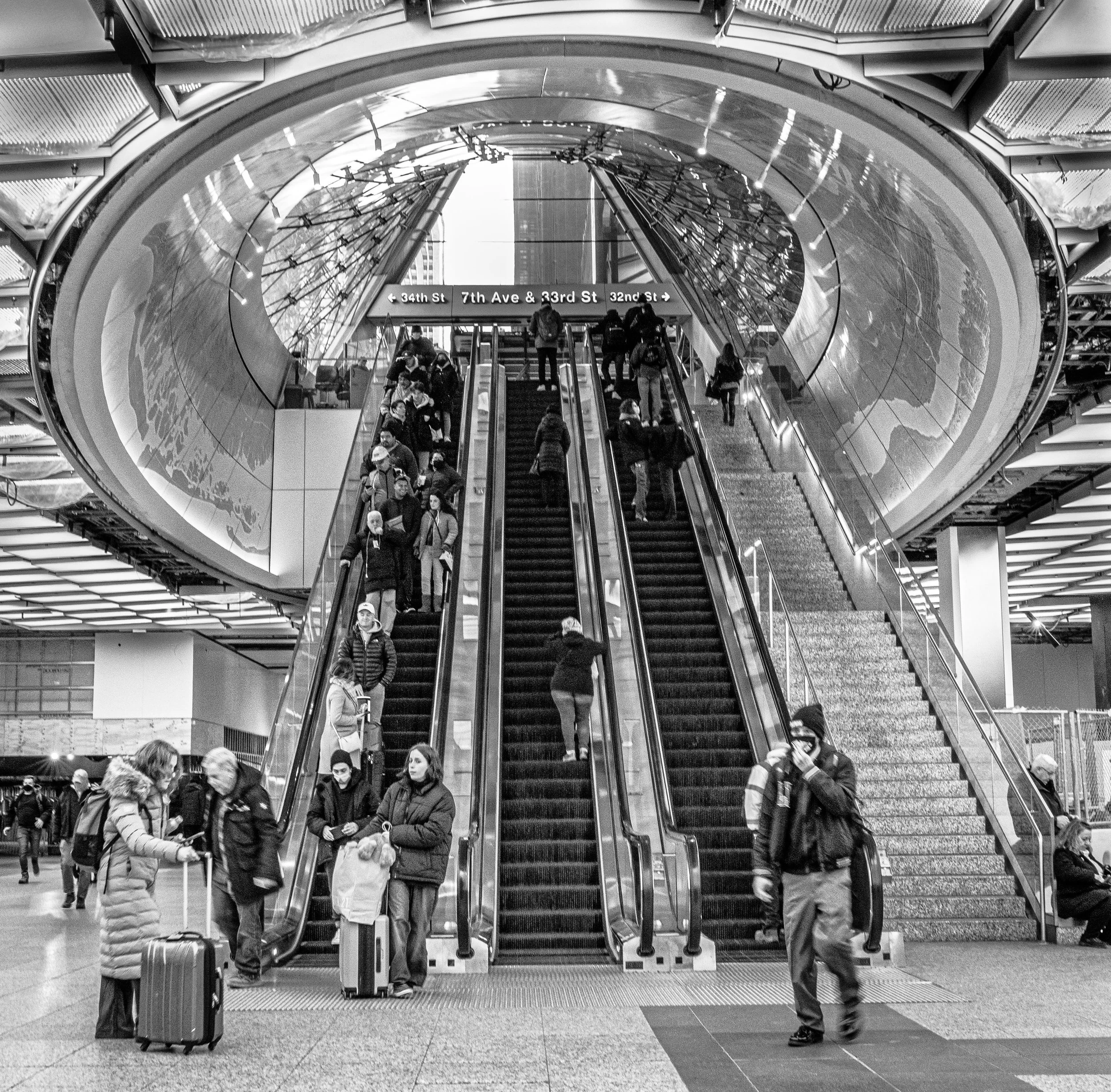 Travelers riding escalators beneath a domed ceiling at a New York City subway station, with signs for 34th Street, 7th Avenue, and 33rd Street.