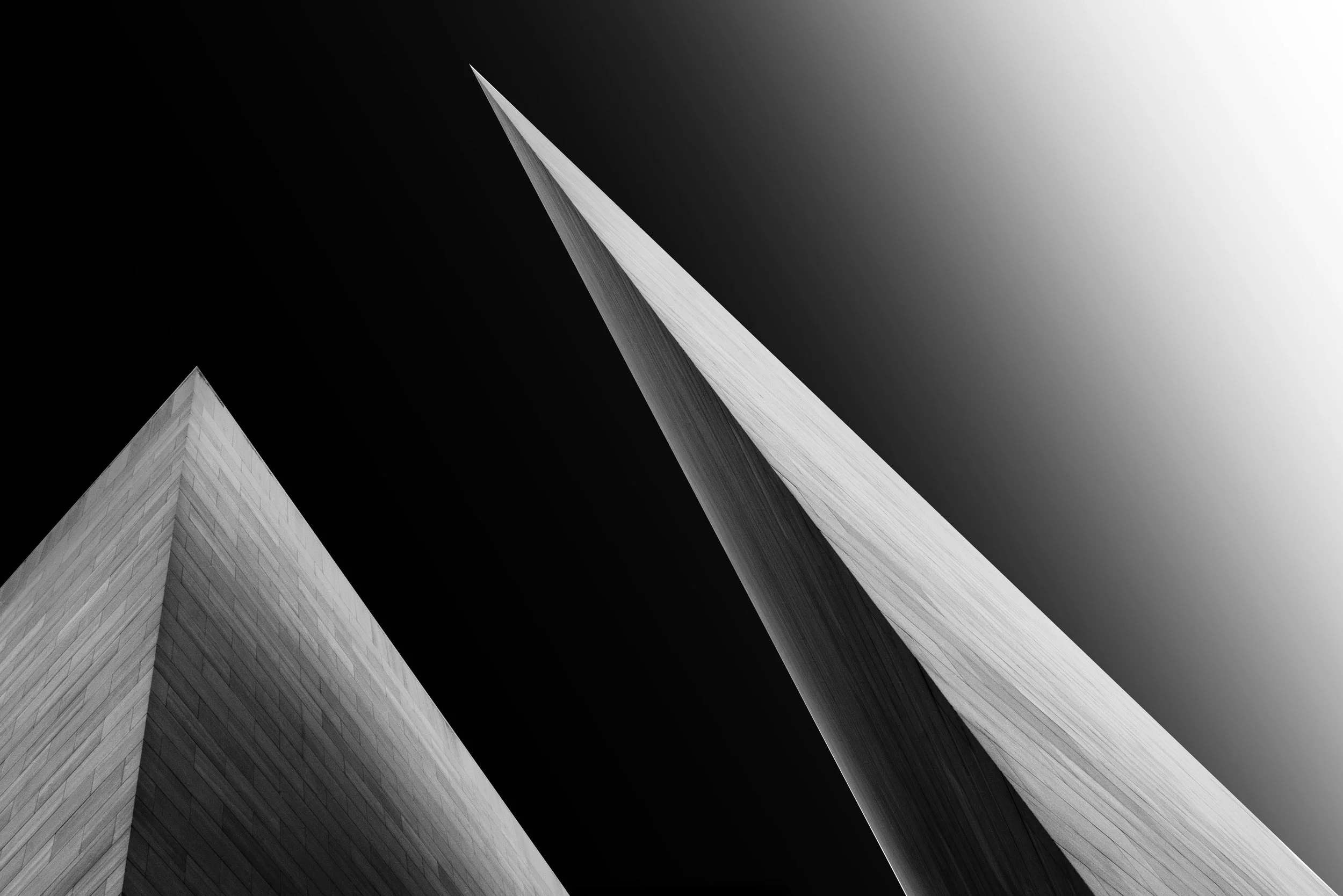 Black-and-white upward view of two sharply pointed modern skyscrapers against a dramatic gradient sky