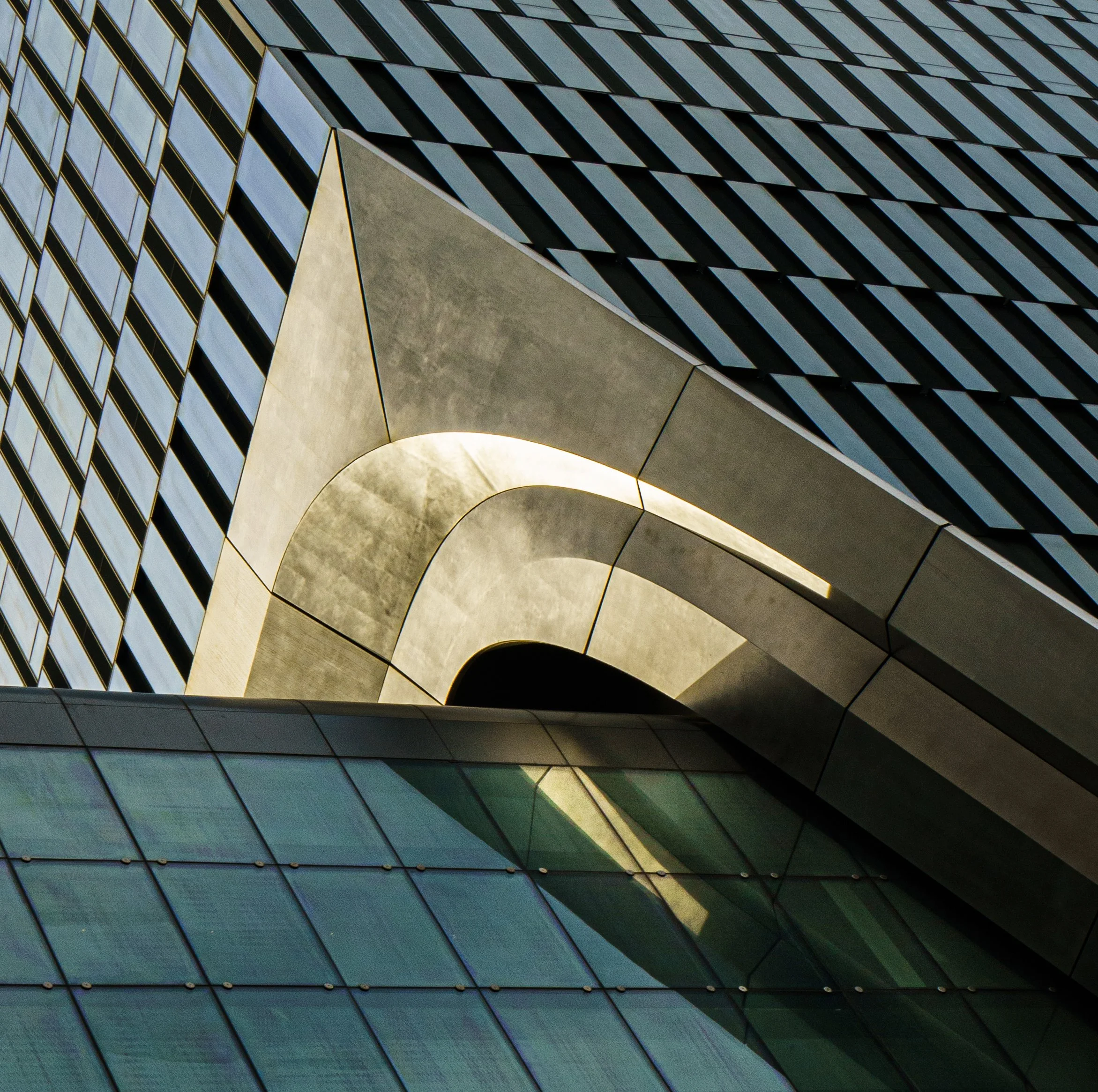 Abstract architectural close-up of overlapping metallic panels and geometric glass windows forming a futuristic building facade.