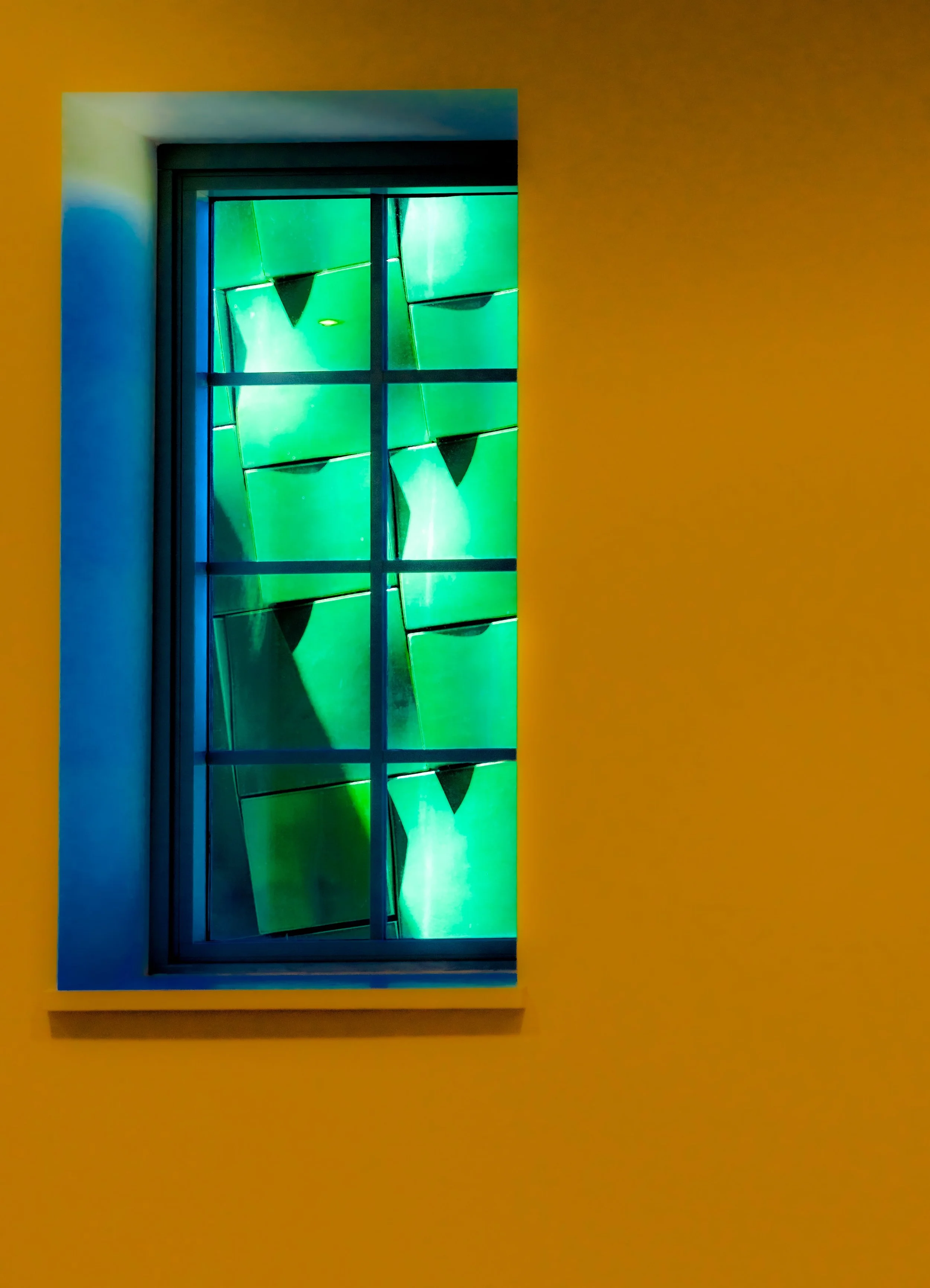 Black-framed window with grid panes and vivid green light, set in an orange wall.