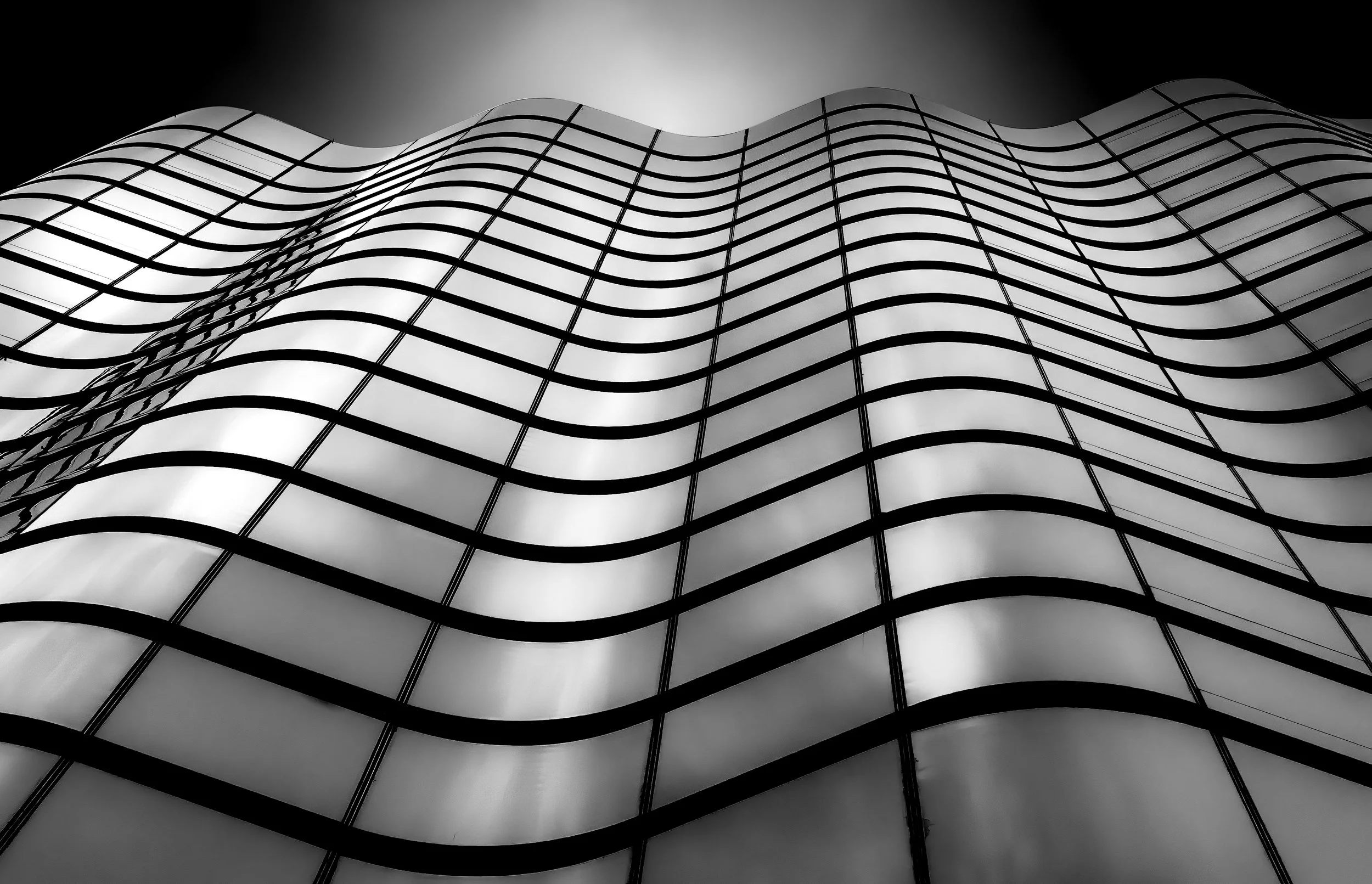 Black-and-white abstract view of a modern glass building facade with undulating grid lines