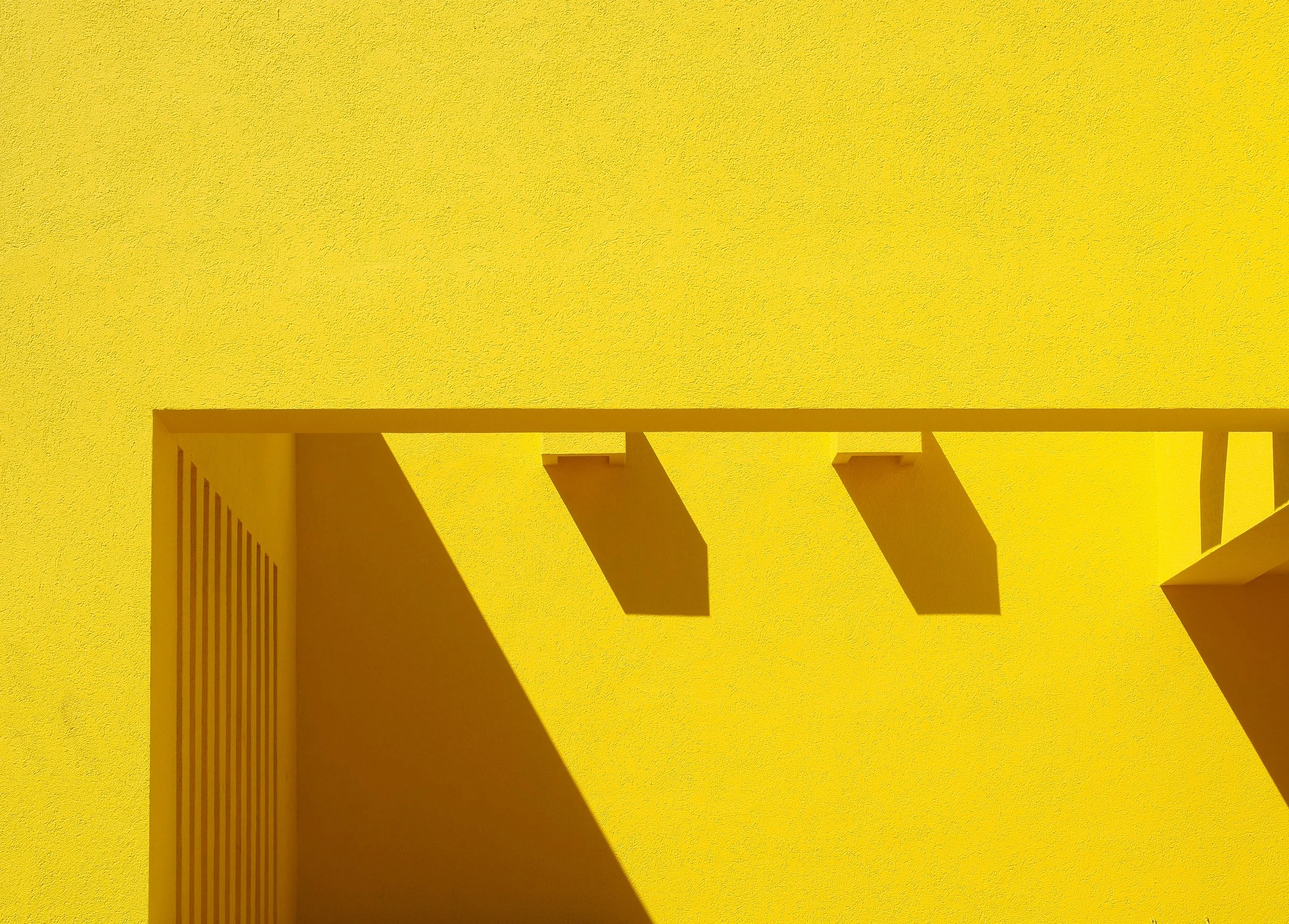 Yellow stucco wall with geometric architectural shadows and a slatted doorway