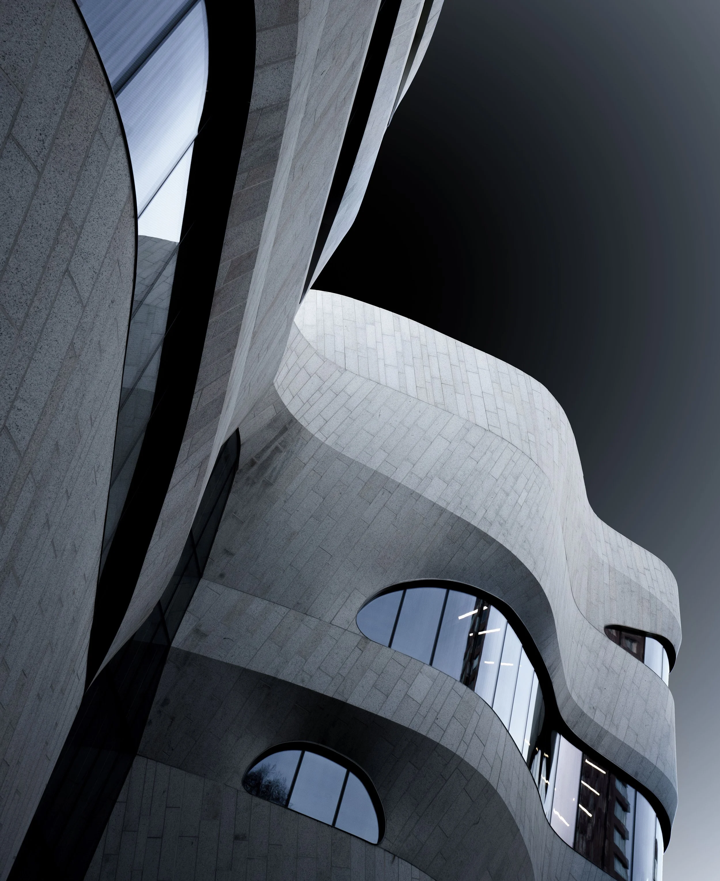 Abstract upward view of a modern white stone building with curved walls, black accents, and arched windows.