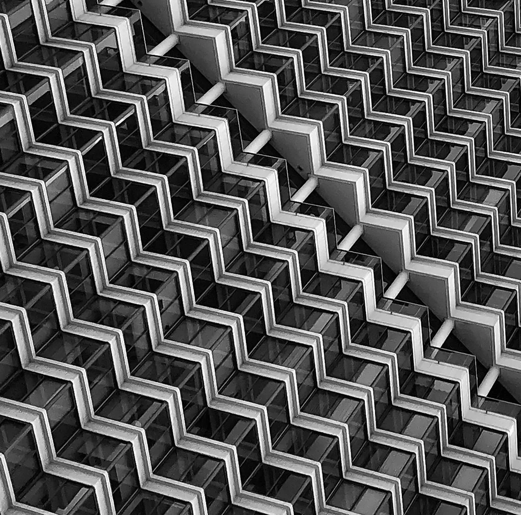 Black-and-white close-up of a modern glass building facade with repeating zigzag architectural patterns