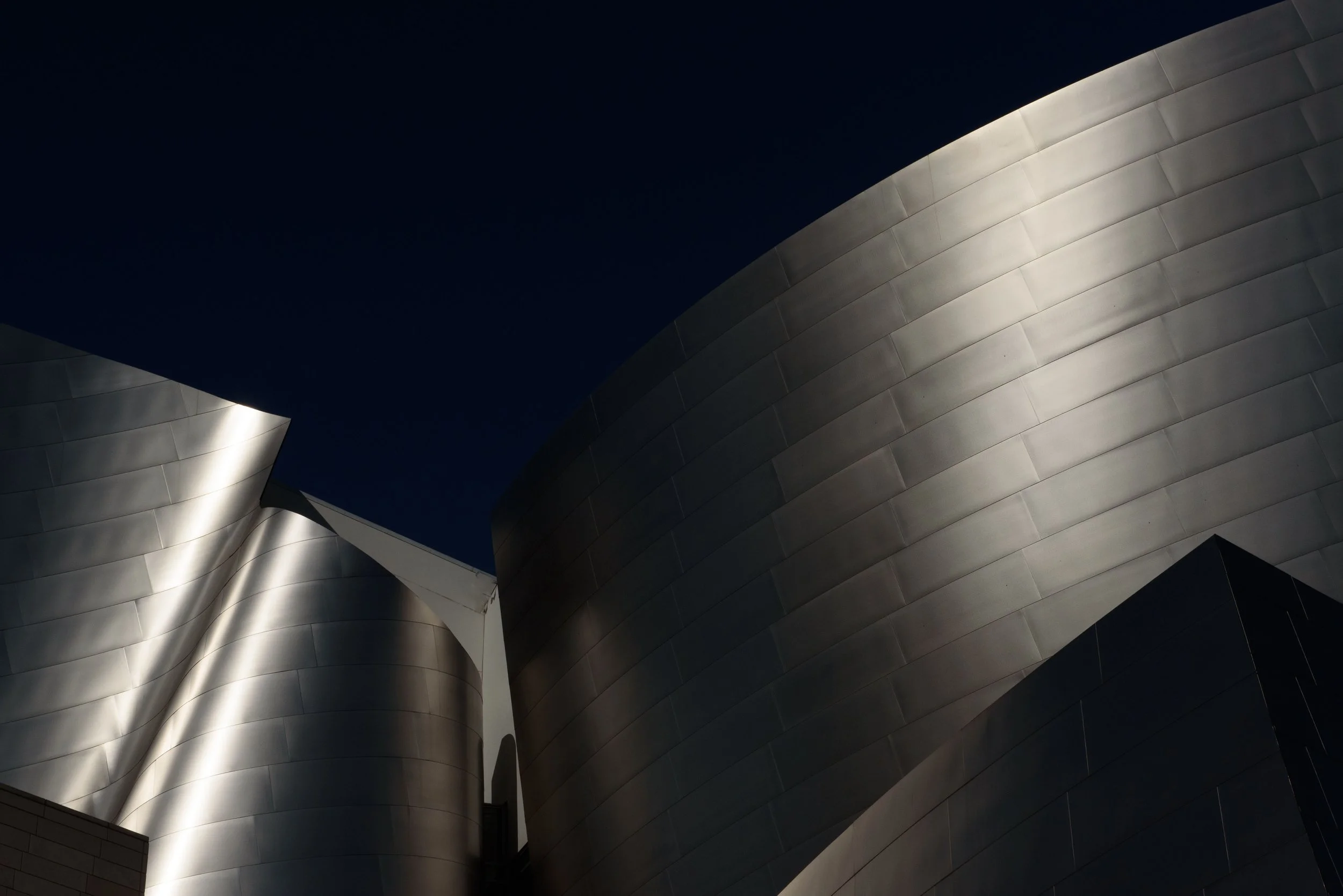 Upward view of illuminated, curved stainless-steel architectural buildings against a dark night sky
