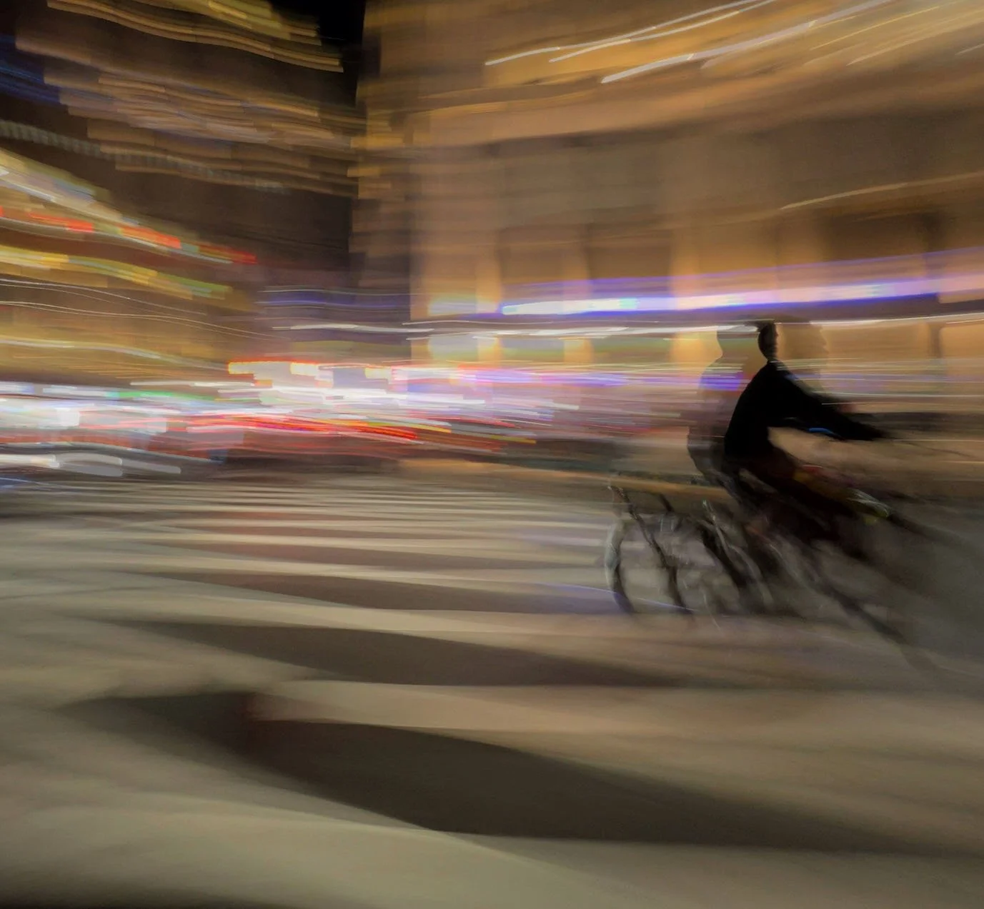 Motion-blurred cyclist riding through a brightly lit city street at night