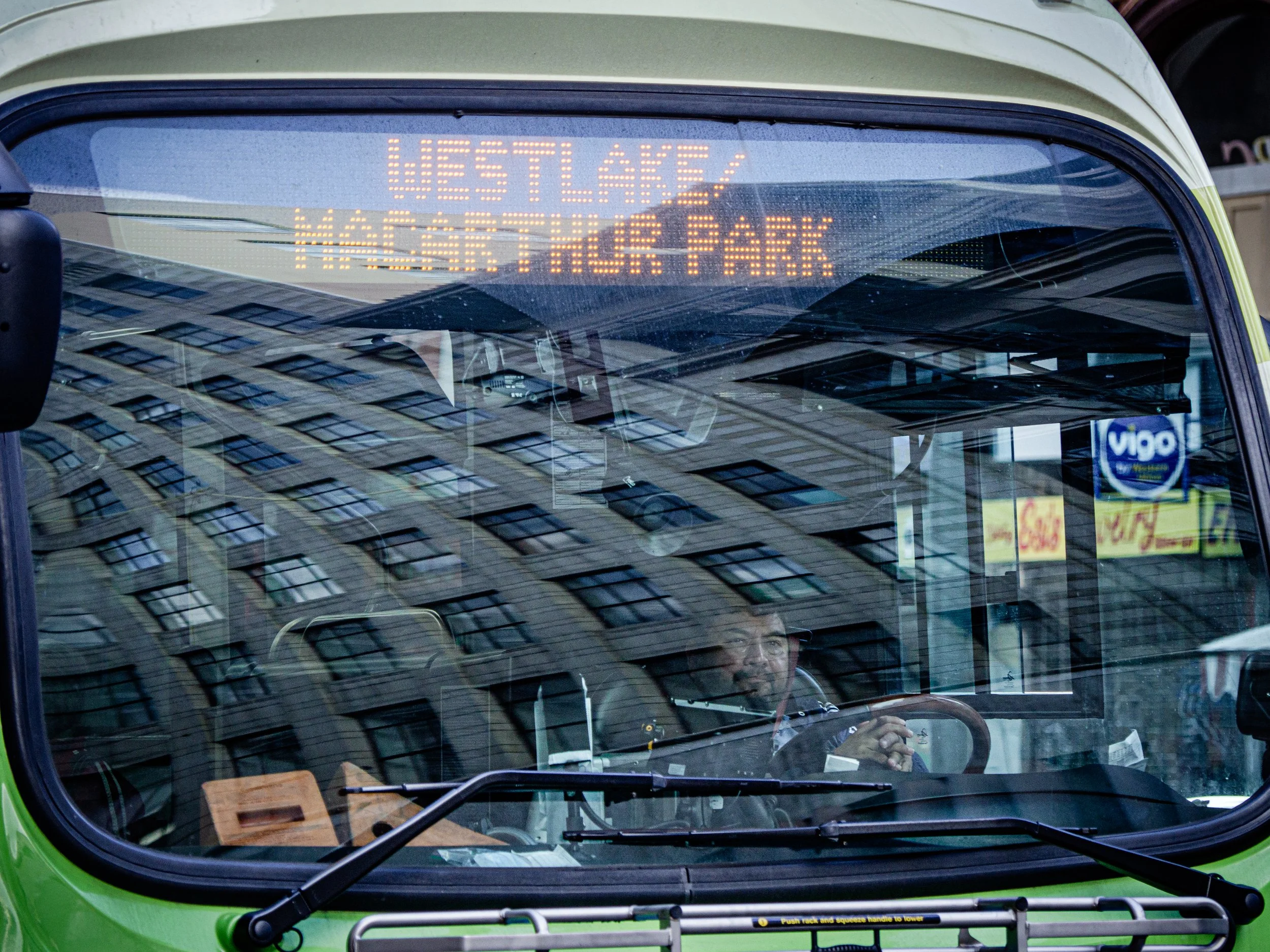 Close-up of a green city bus windshield displaying the LED destination sign “Ligne 7 – 4 septembre,” with the driver visible inside.