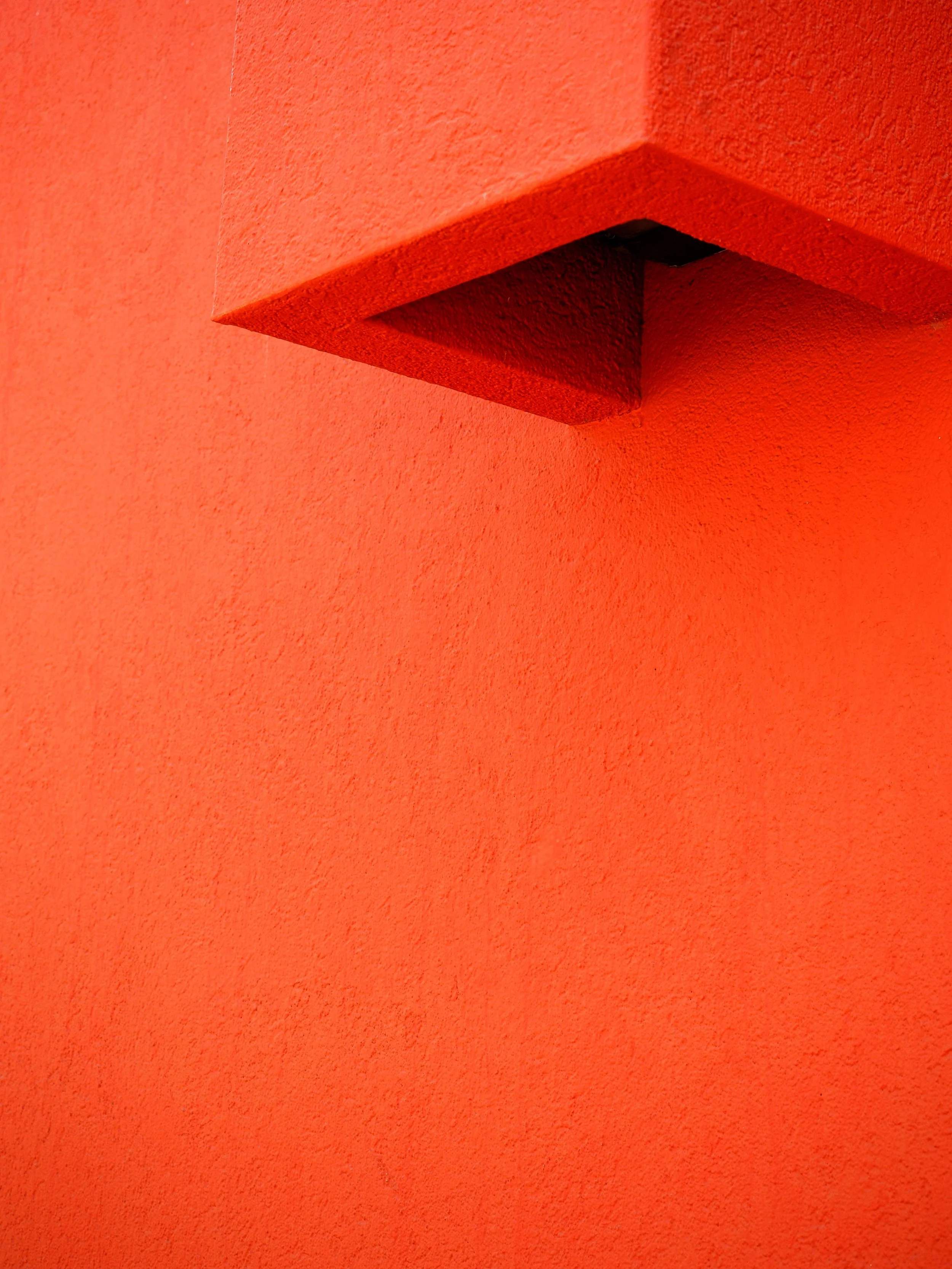 Close-up of a red-painted concrete ledge and textured wall corner with a dark rectangular opening underneath