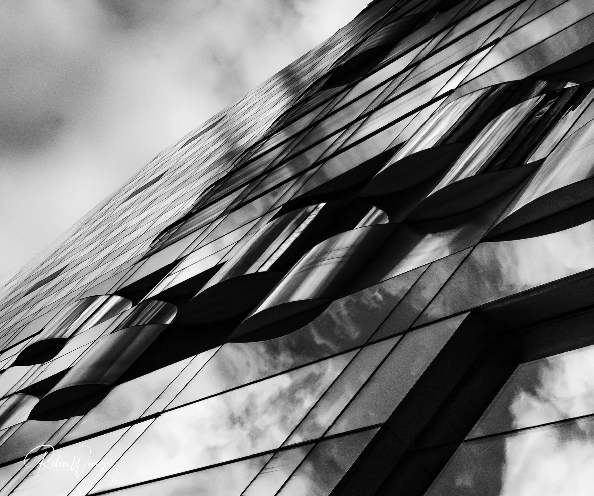 Black-and-white abstract close-up of angular glass building reflections and geometric facade patterns