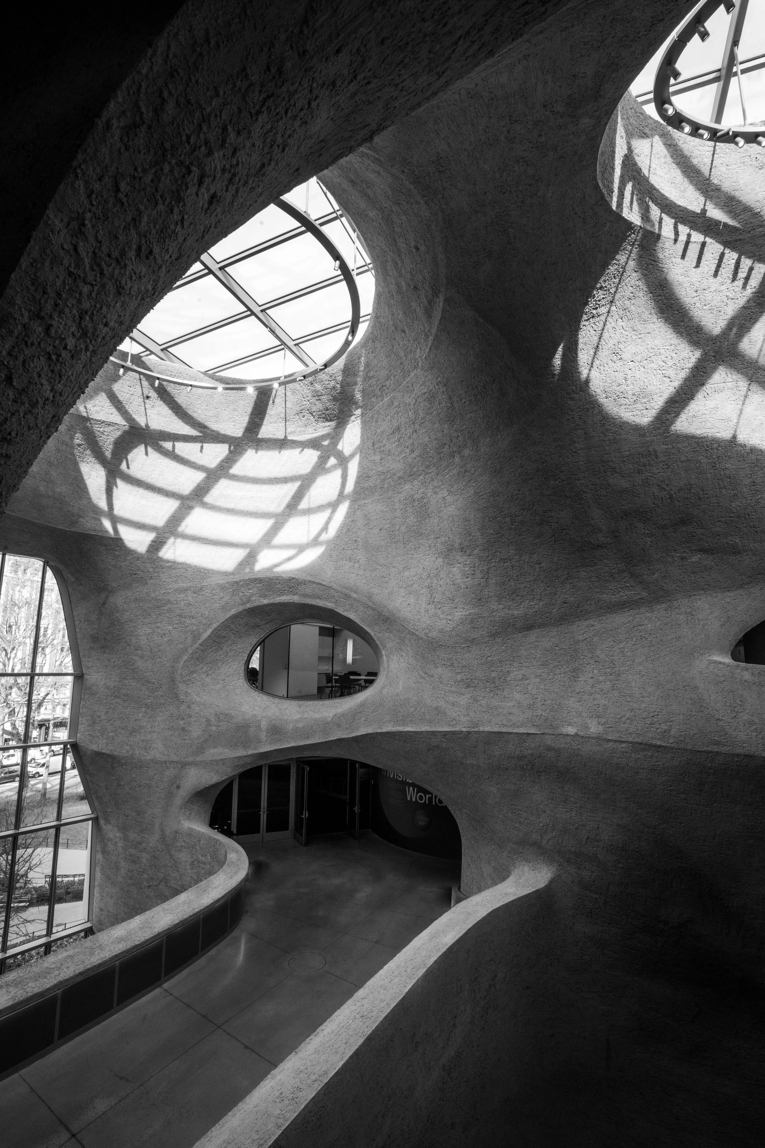 Black-and-white interior of an organic, cave-like building with curved textured walls, skylights, and circular windows