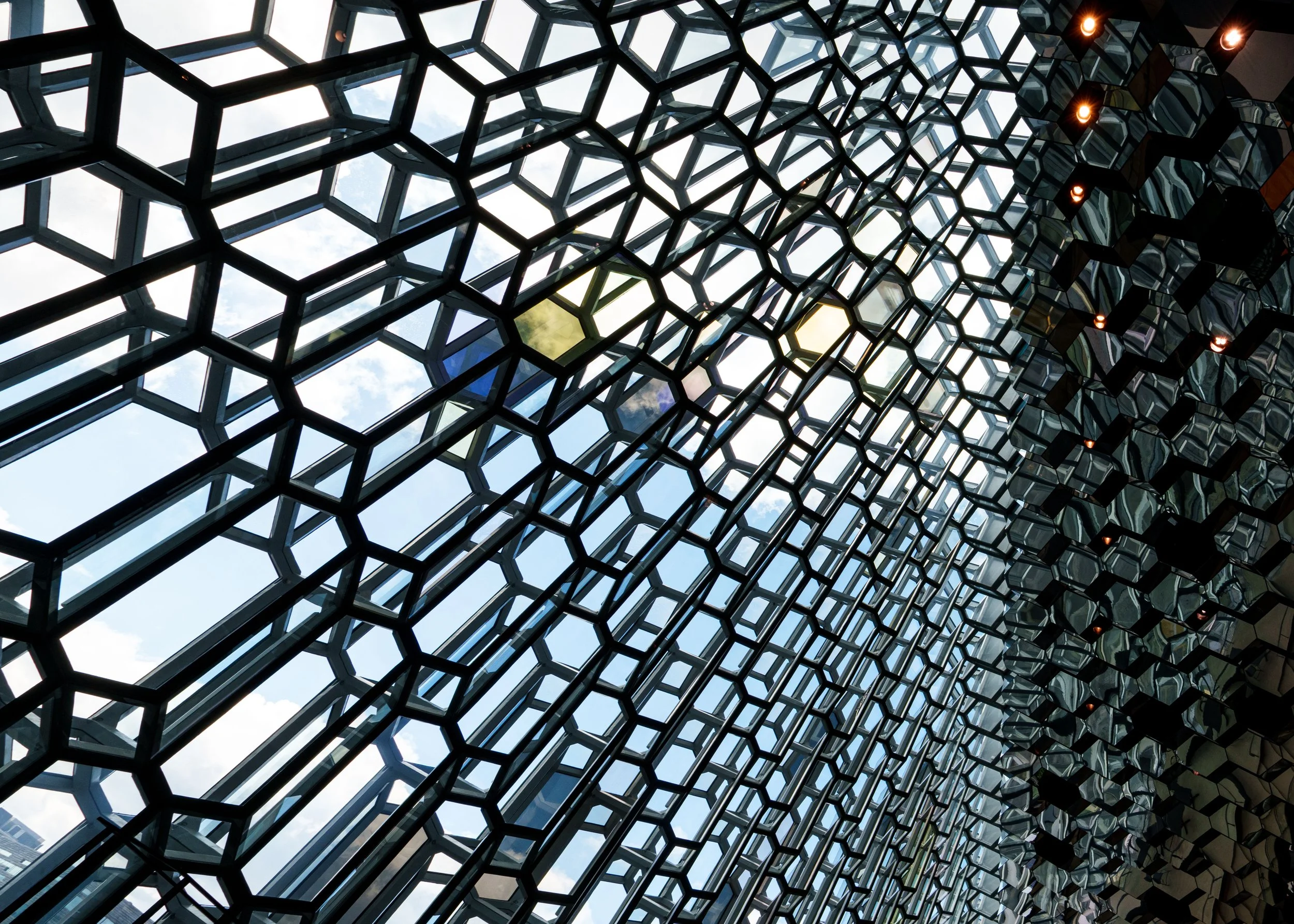 Geometric glass ceiling with a honeycomb-patterned steel frame and blue sky visible above