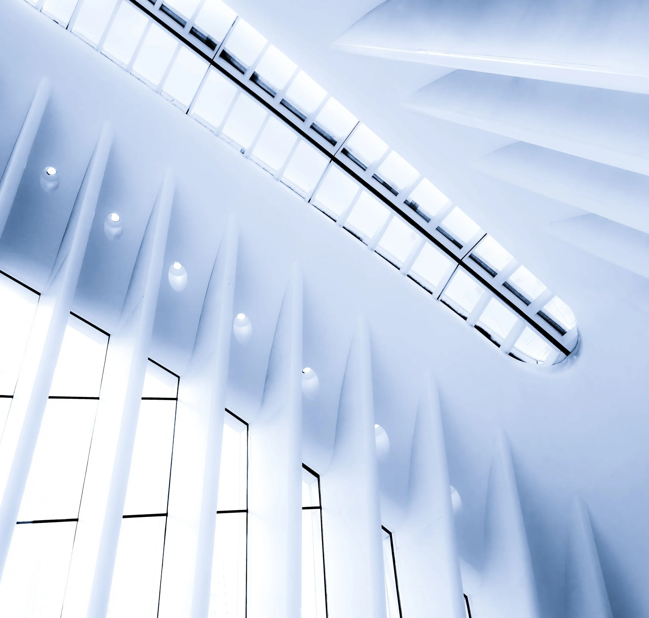 Abstract view of a bright white modern atrium with skylights, tall columns, and recessed ceiling lights
