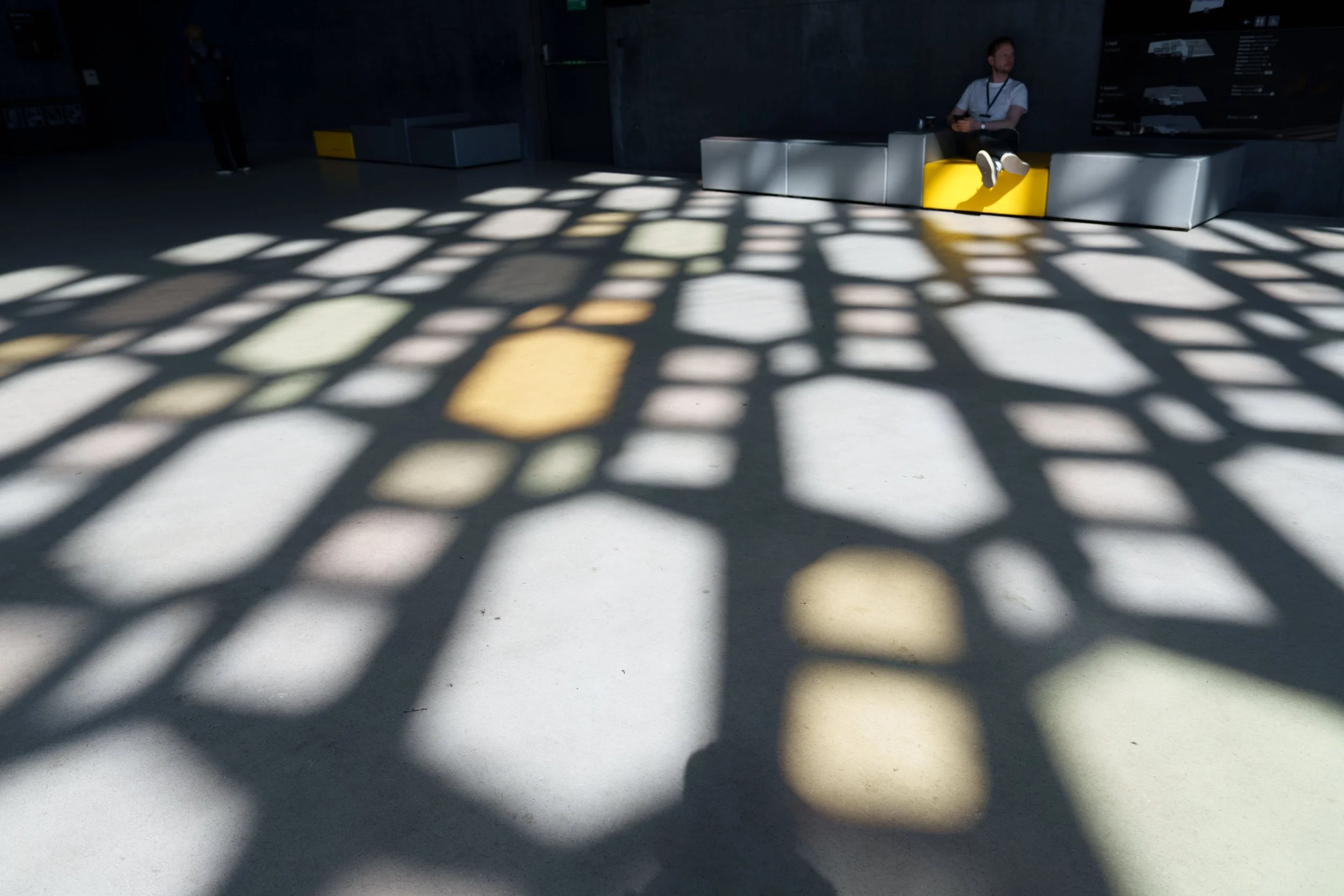 Museum interior with colorful geometric window shadows across the floor and a person seated on a bench