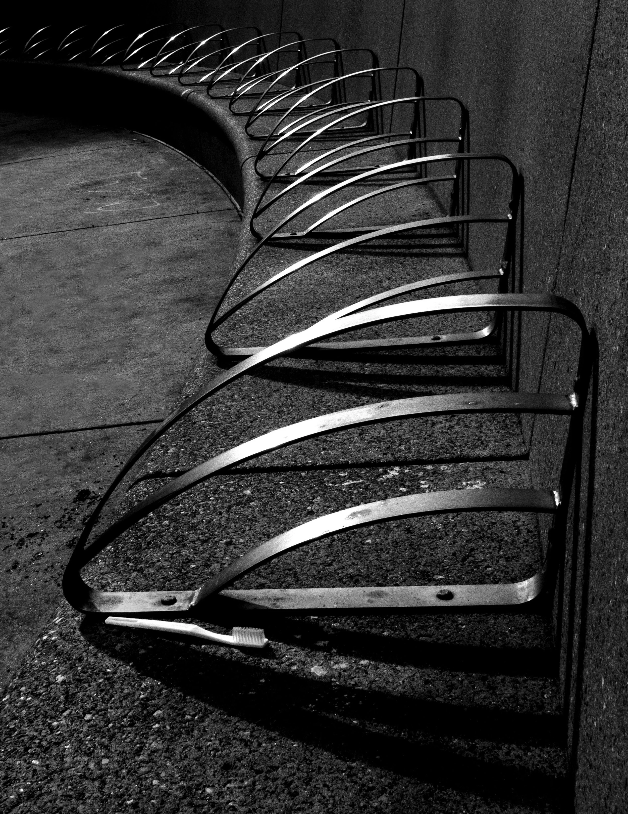 Black-and-white close-up of rows of metal chairs along a wall, with a toothbrush on the floor beneath them