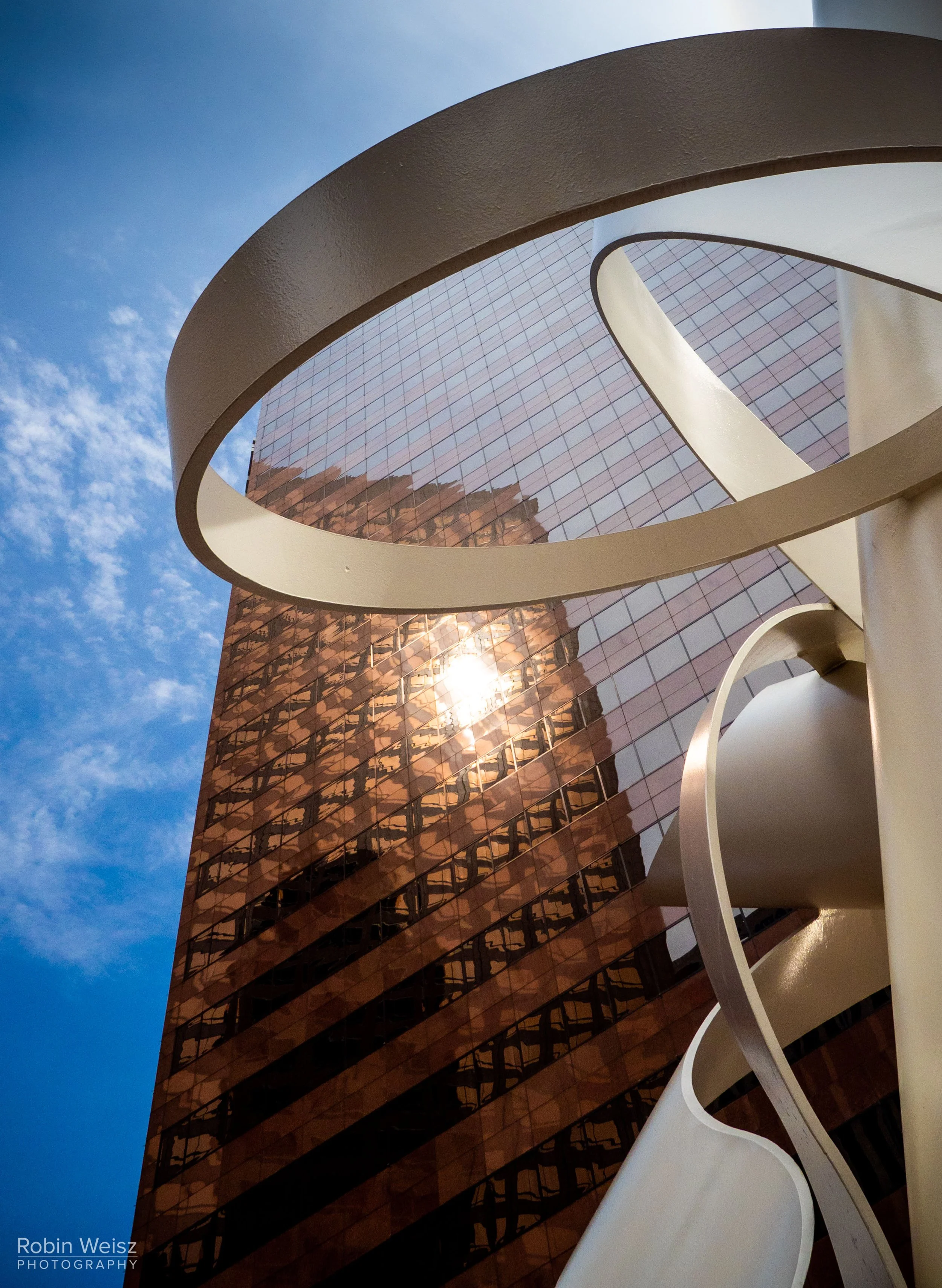 Low-angle view of a reflective glass office building framed by sweeping white architectural arches under a blue sky