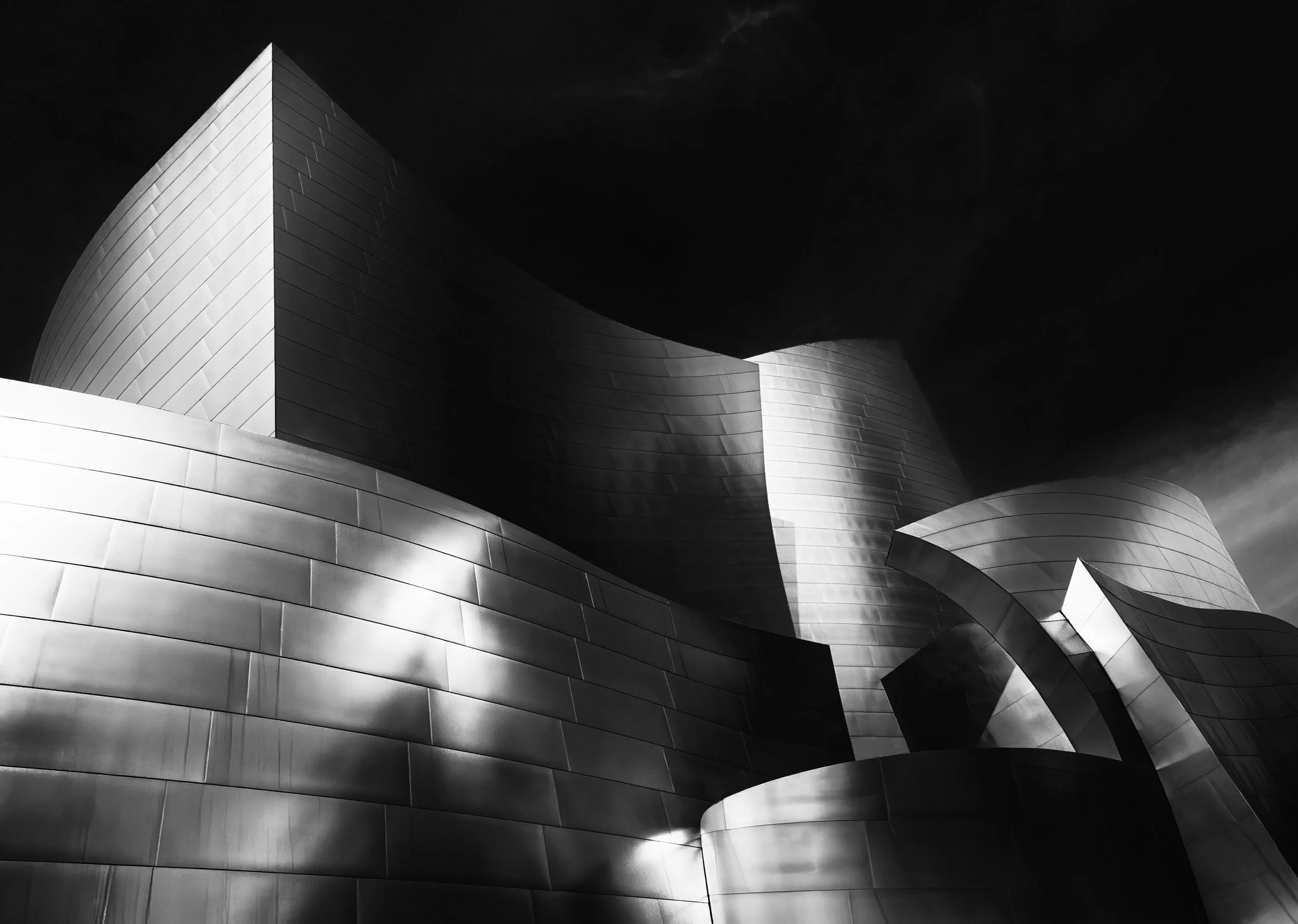 Black-and-white low-angle view of the Walt Disney Concert Hall’s sweeping stainless steel curves against a dark sky