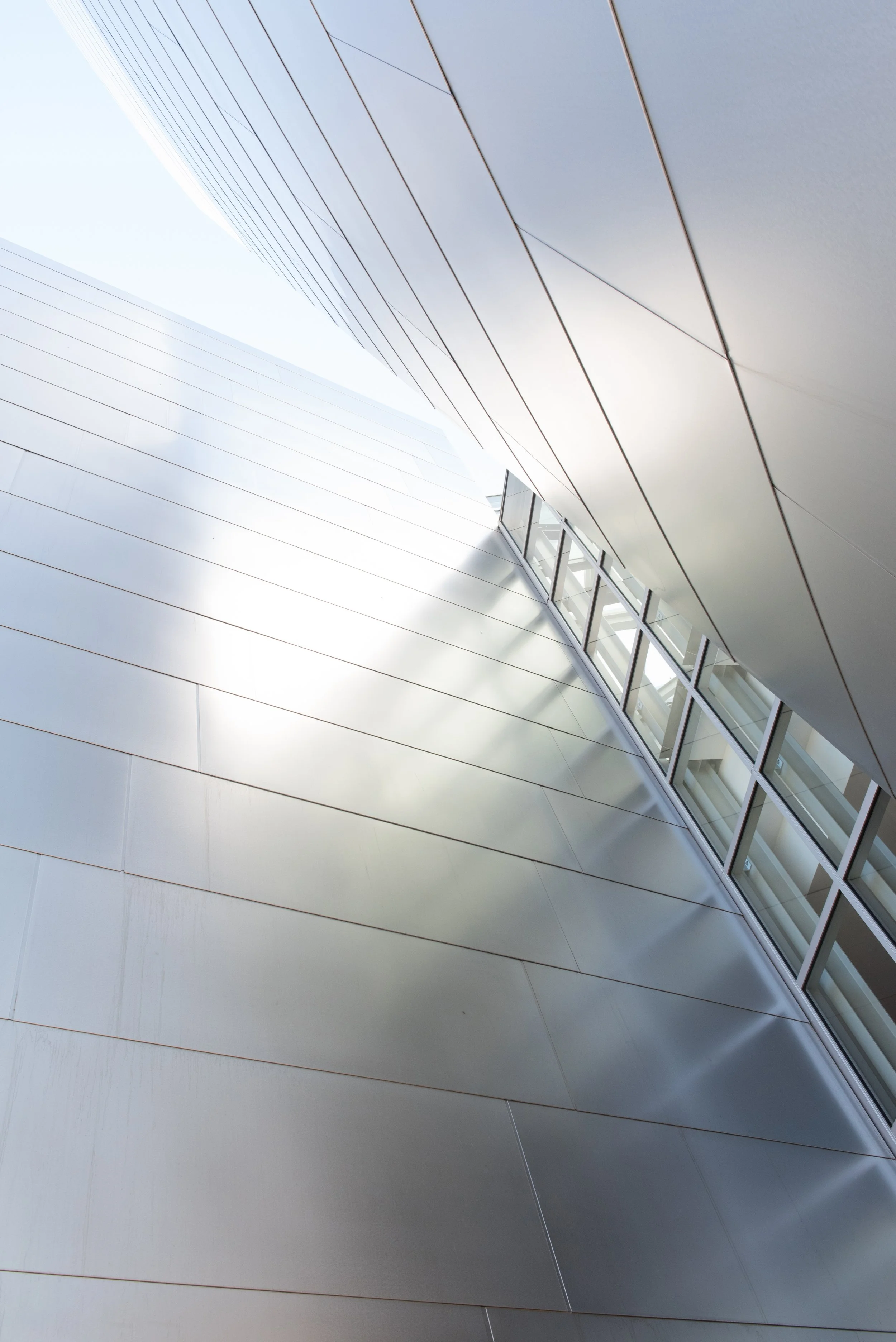 Abstract upward view of a modern building’s white paneled architecture and curved glass windows
