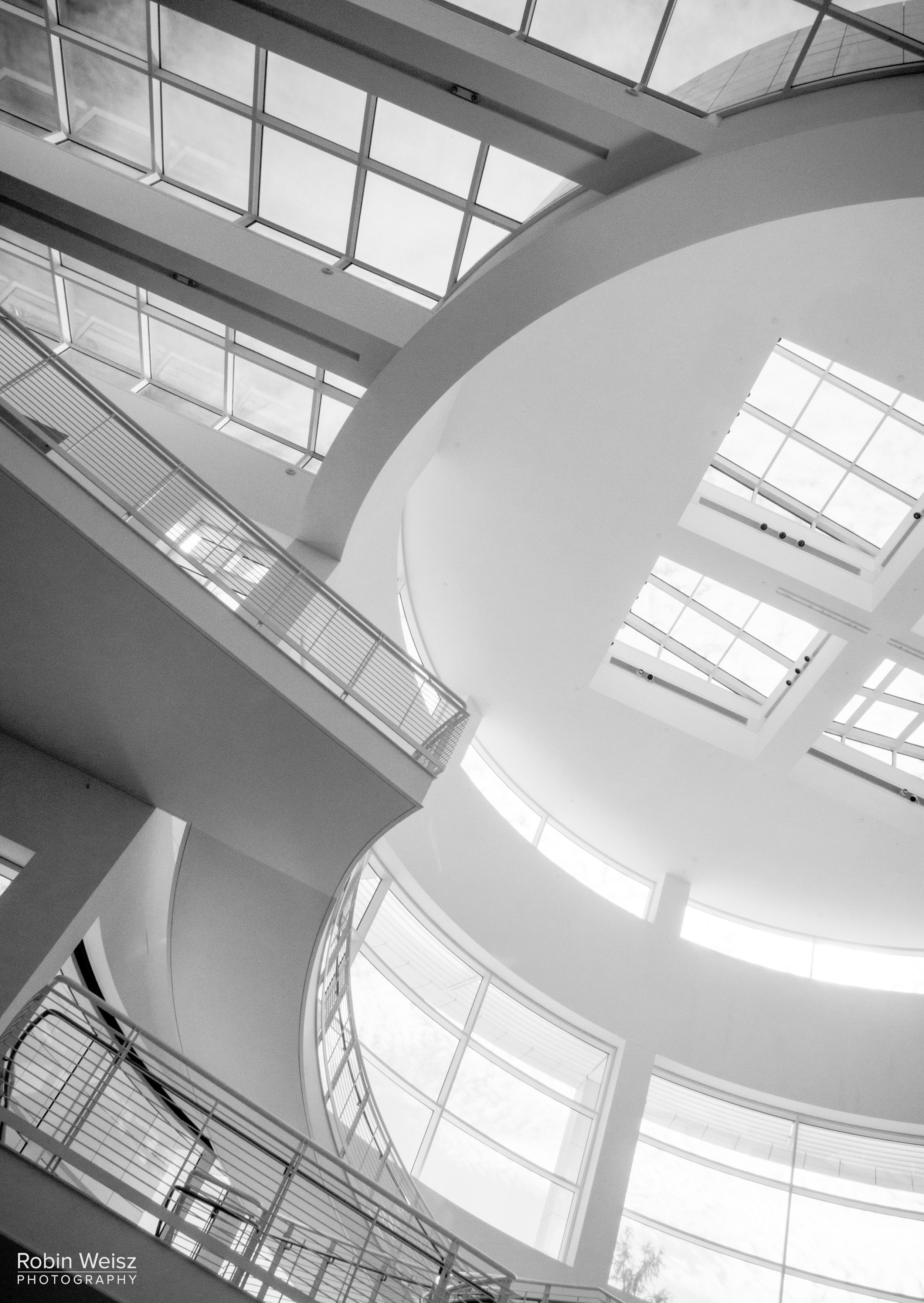 Black-and-white view of a modern atrium with skylights, white structural beams, and metal stair railings.
