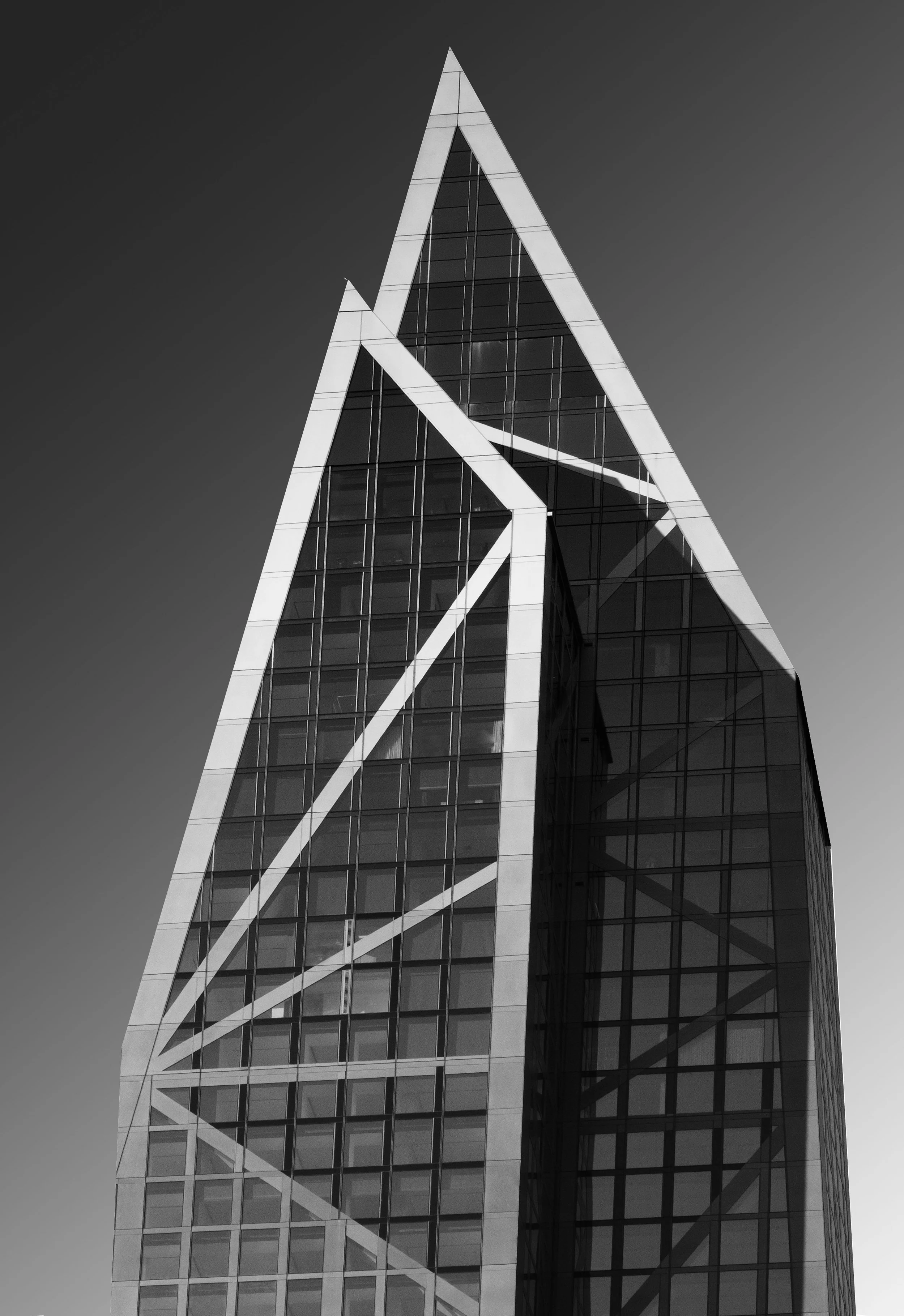 Black-and-white close-up of a modern glass office skyscraper with dramatic white diagonal structural beams against a dark sky