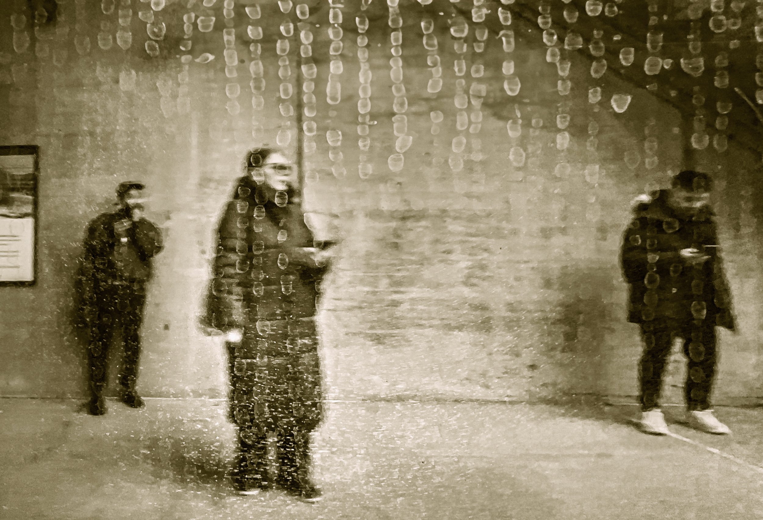 Sepia-toned photo of three people standing beneath a wall covered in raindrops or water droplets.