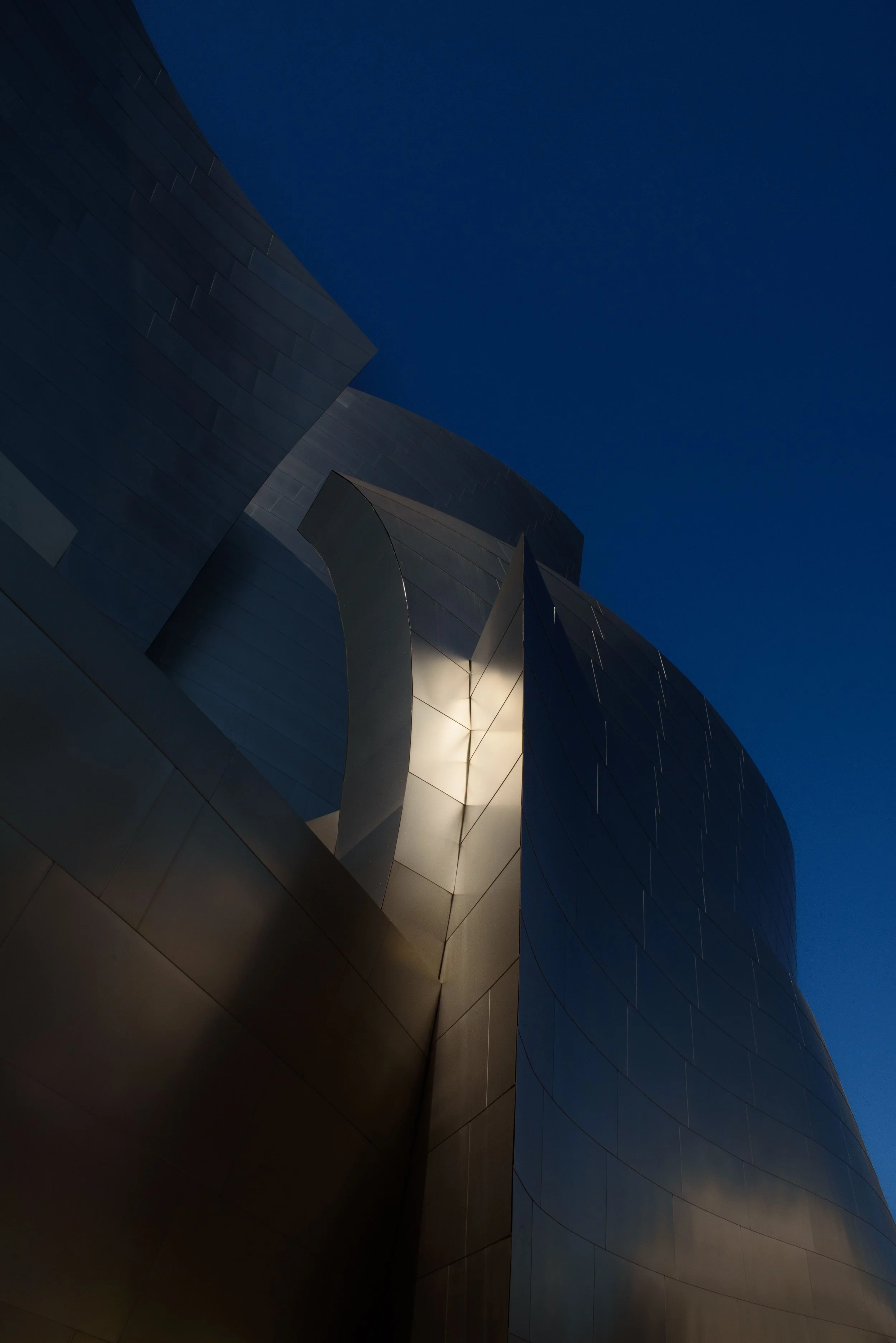 Low-angle view of a modern angular metal building facade against a deep blue sky